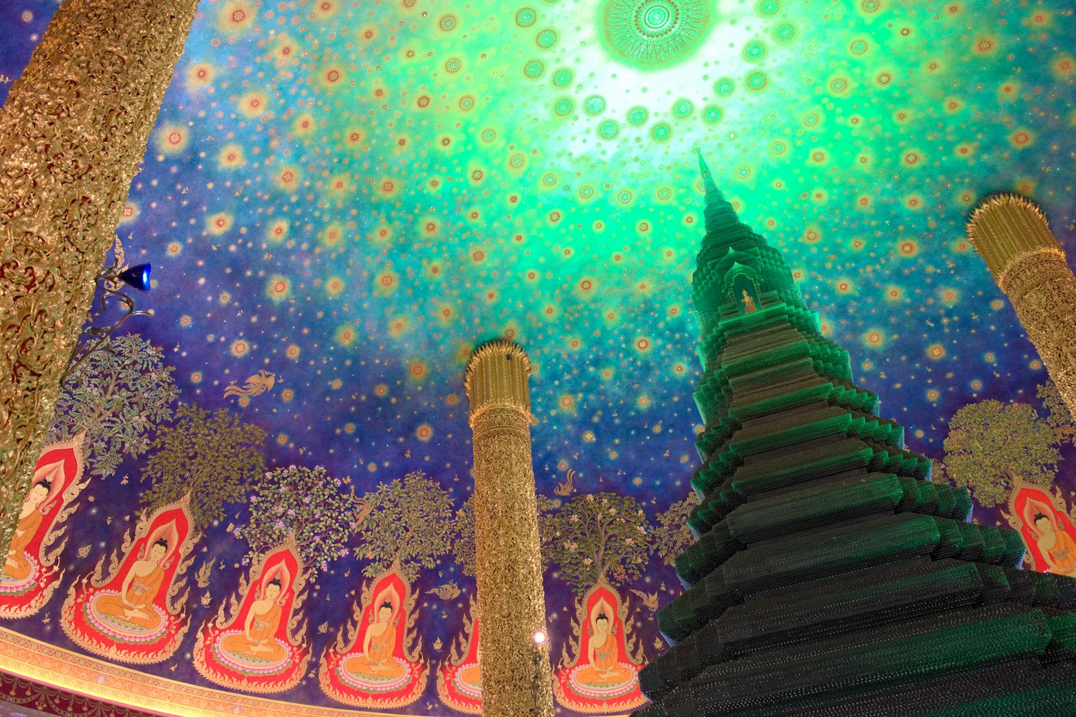 Interior de un templo con un techo decorativo e iluminación verde que presenta estatuas de Buda