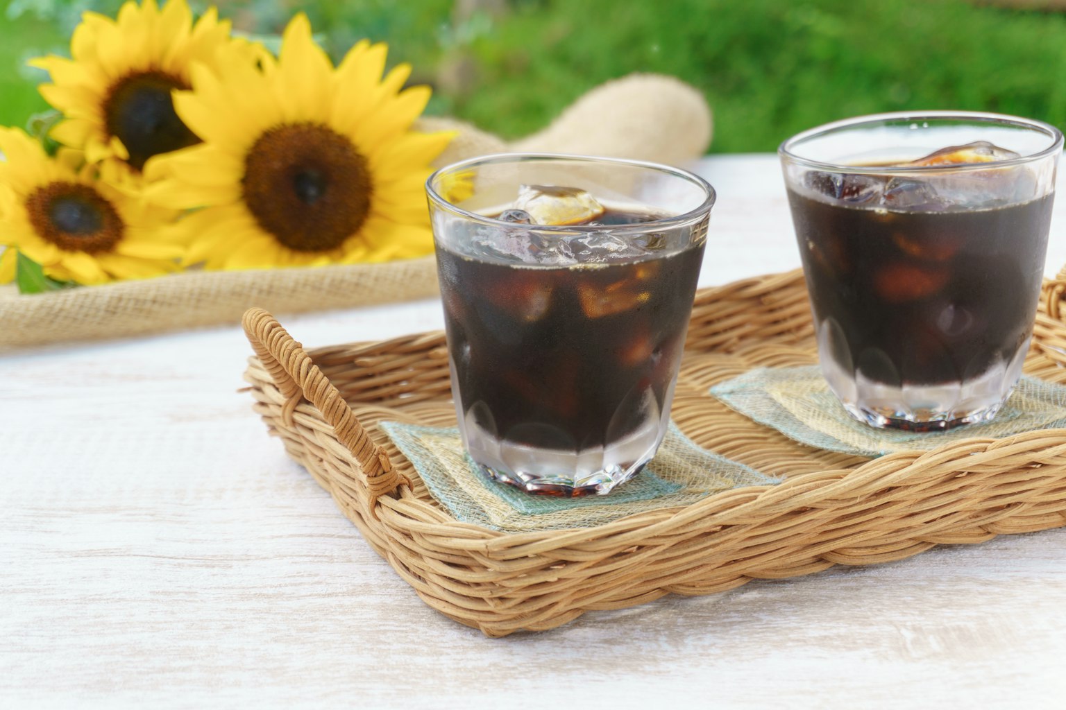 Due bicchieri di caffè freddo su un vassoio di paglia con girasoli sullo sfondo