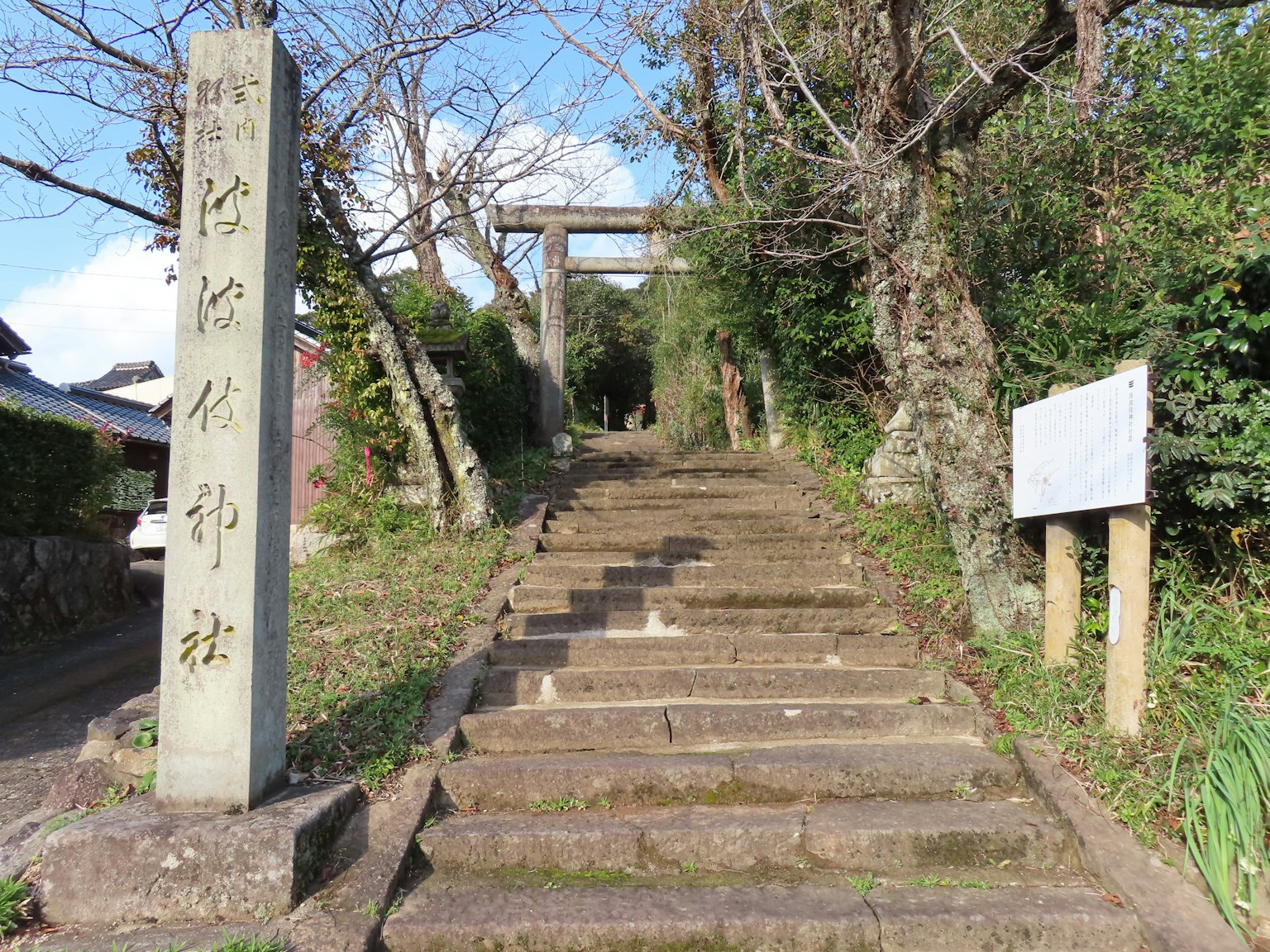 Un camino de piedra que lleva a un santuario con una puerta torii y un letrero