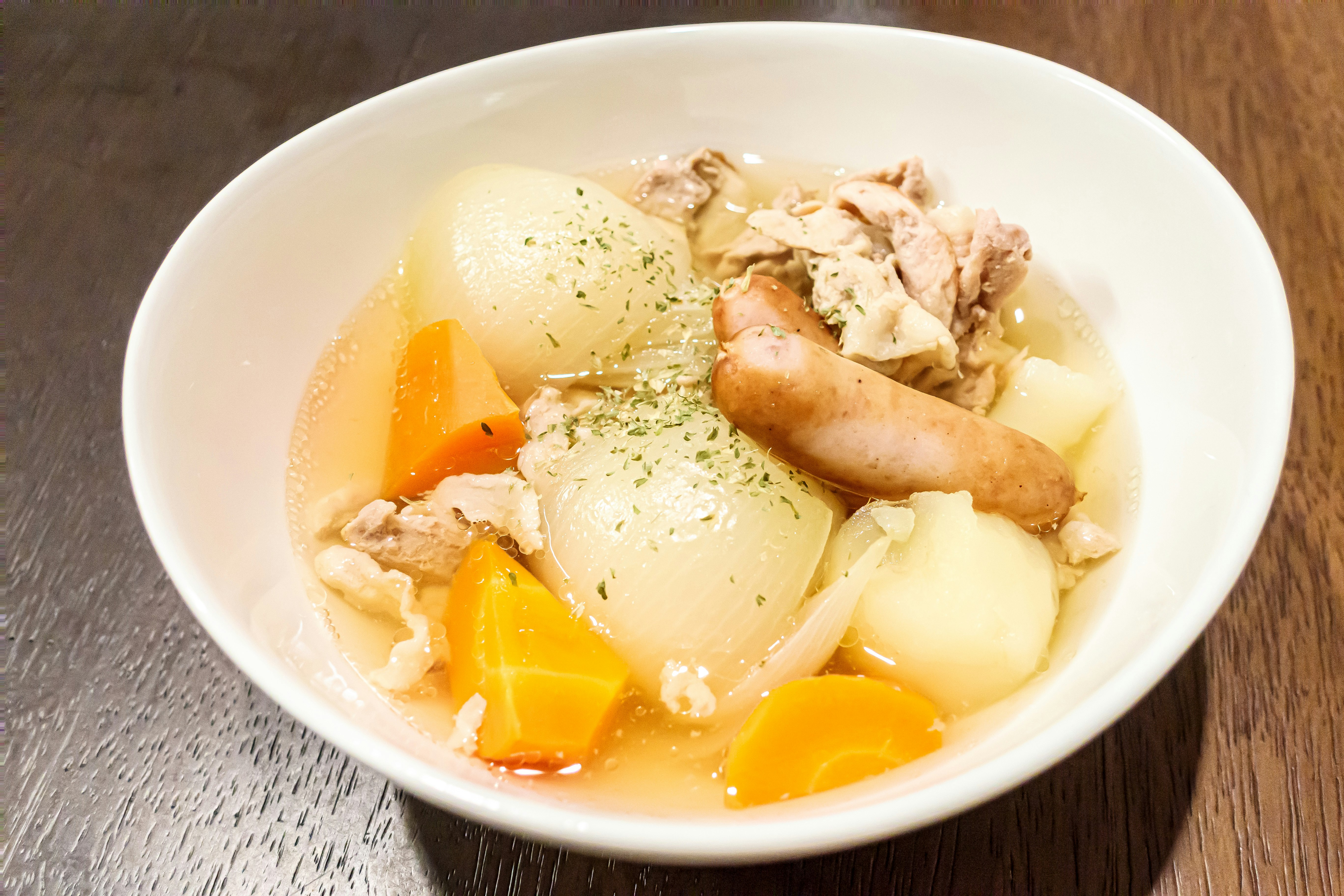 ポトフのスープボウルに浮かぶ野菜とソーセージ