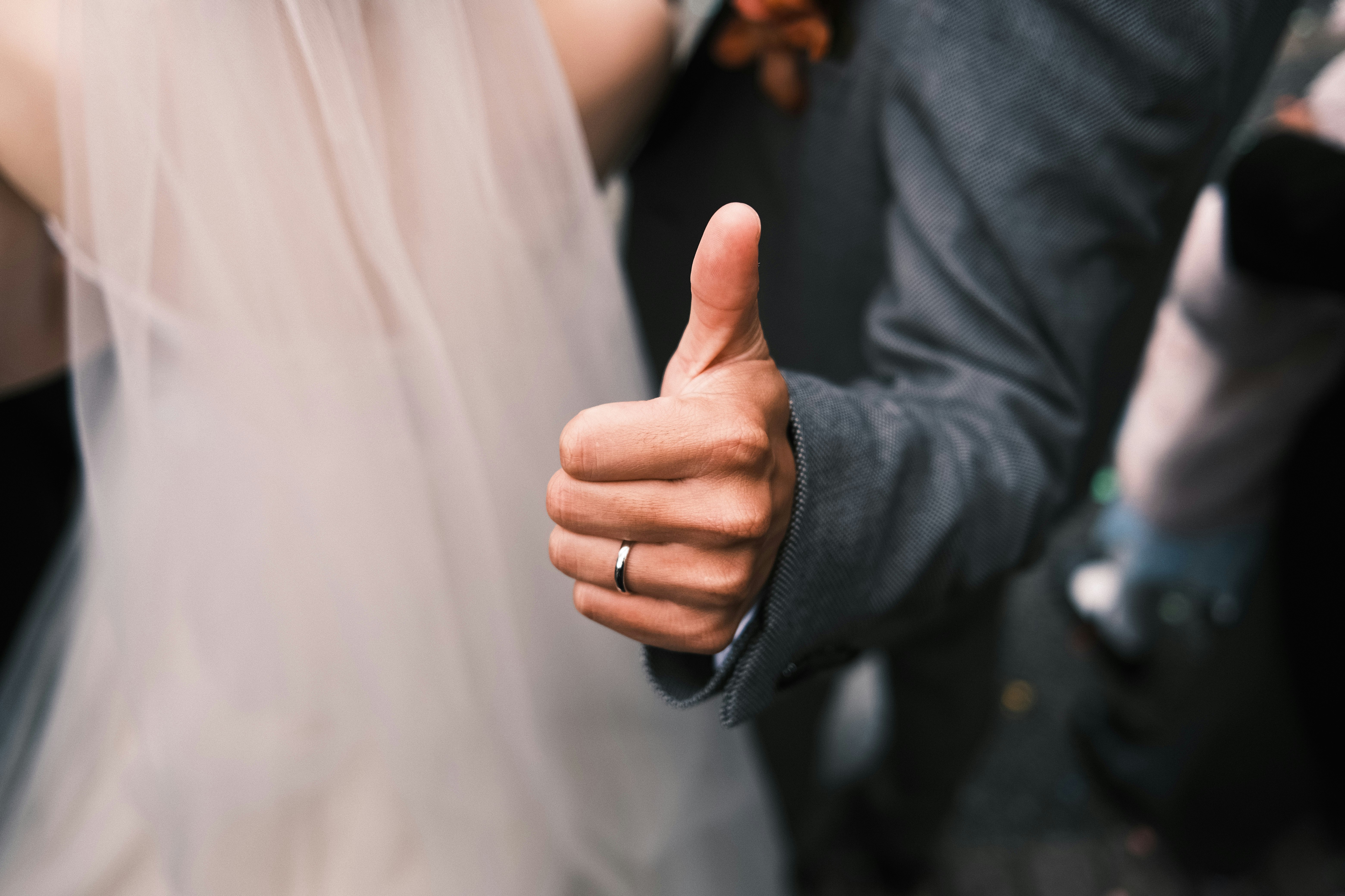 親指を立てる手と結婚衣装のカップル