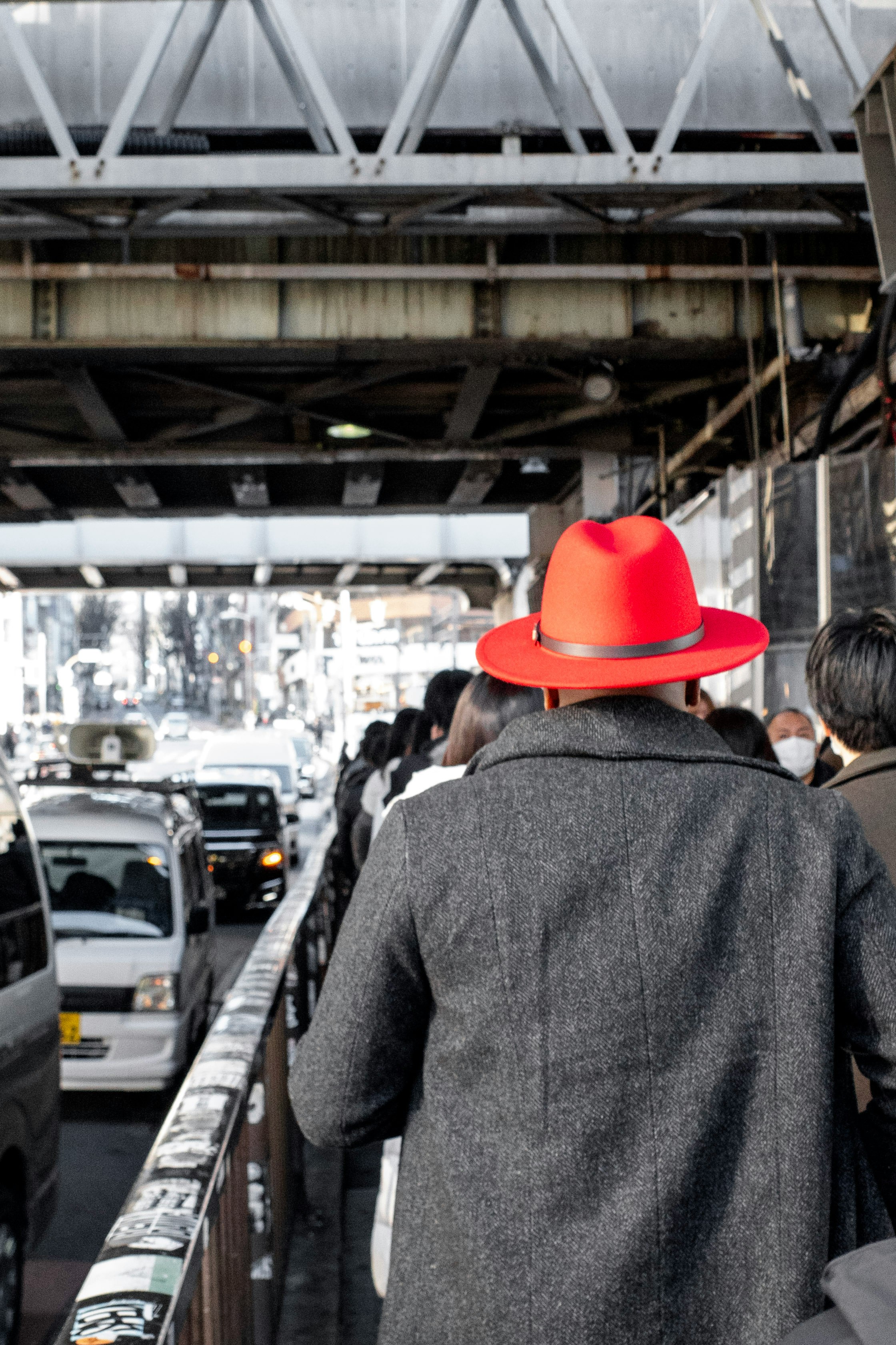 高架下の車列と赤い帽子の背中が並ぶ通りの人混み