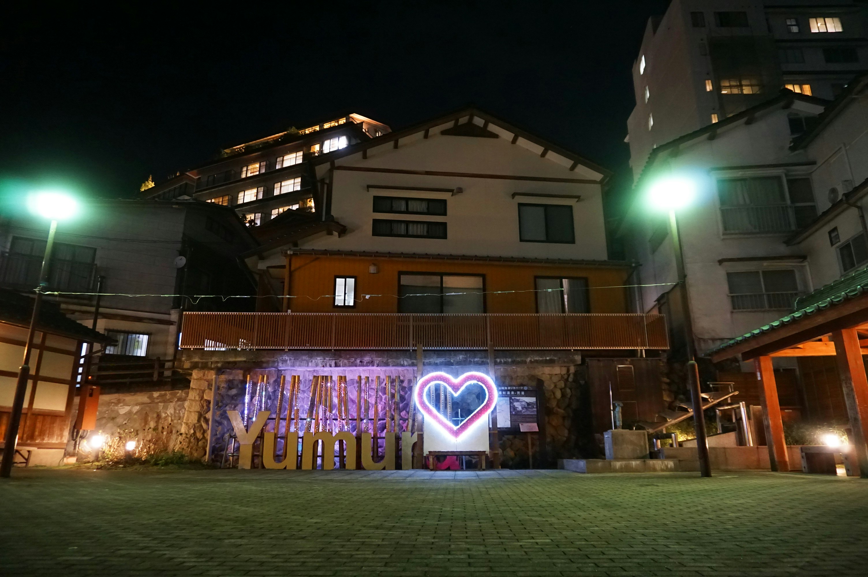 夜の中庭で光るハート型ネオンと「Yumu」看板のある建物