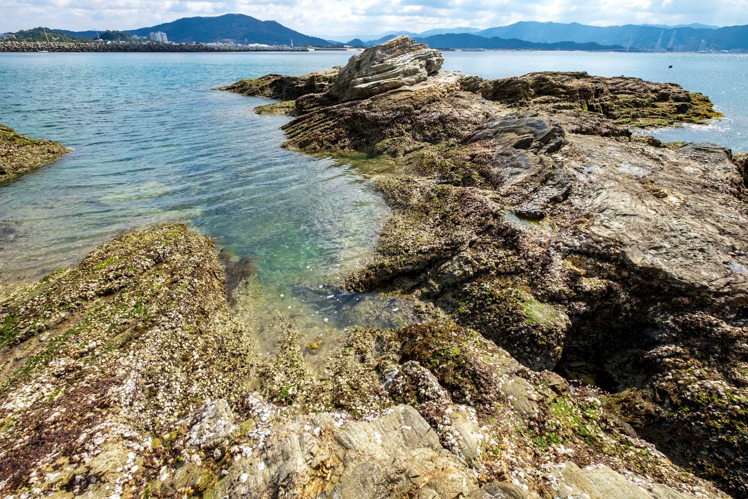 Paesaggio costiero roccioso con acqua limpida e colline in lontananza
