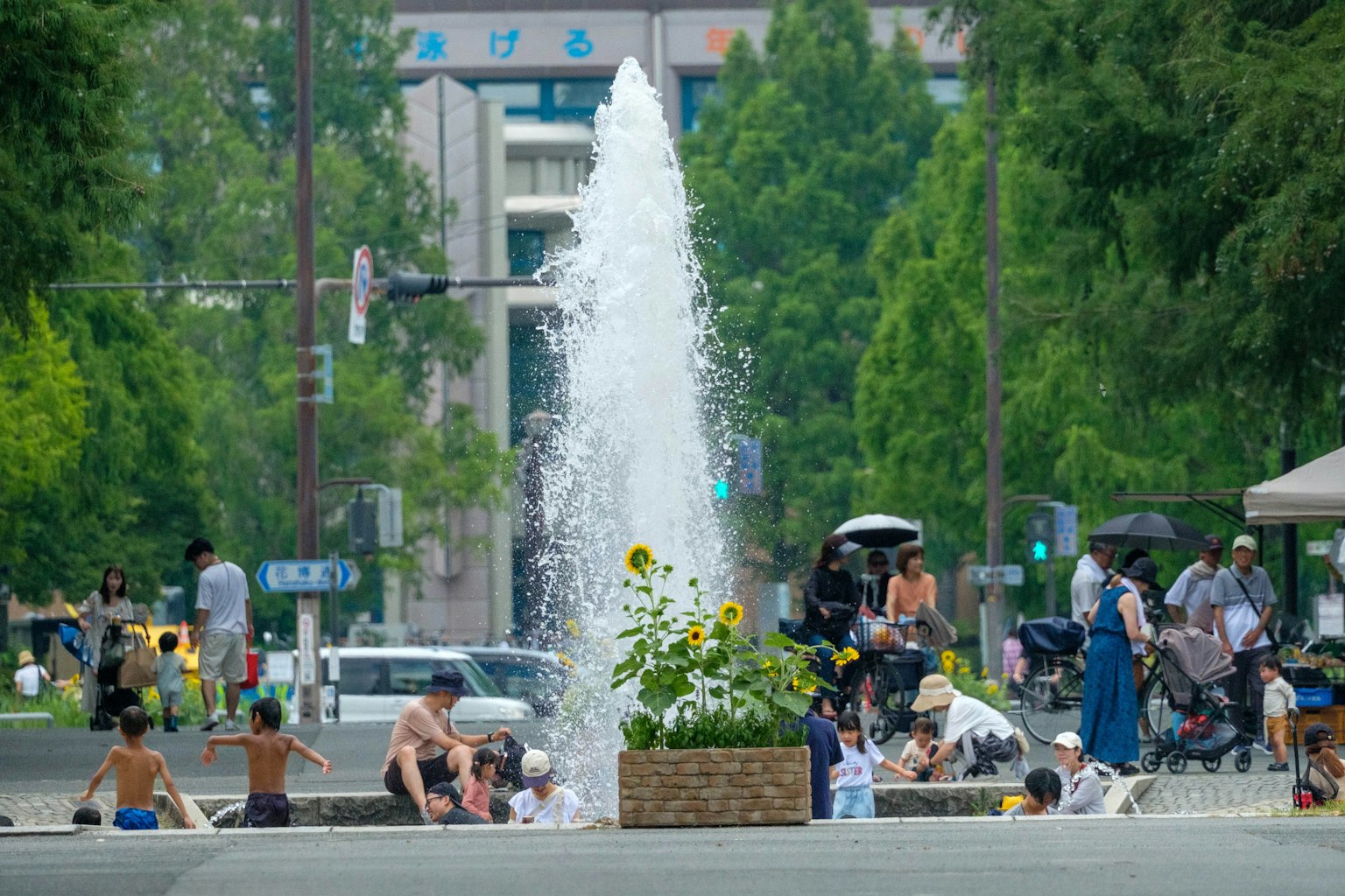 Children and adults enjoying a park fountain surrounded by greenery