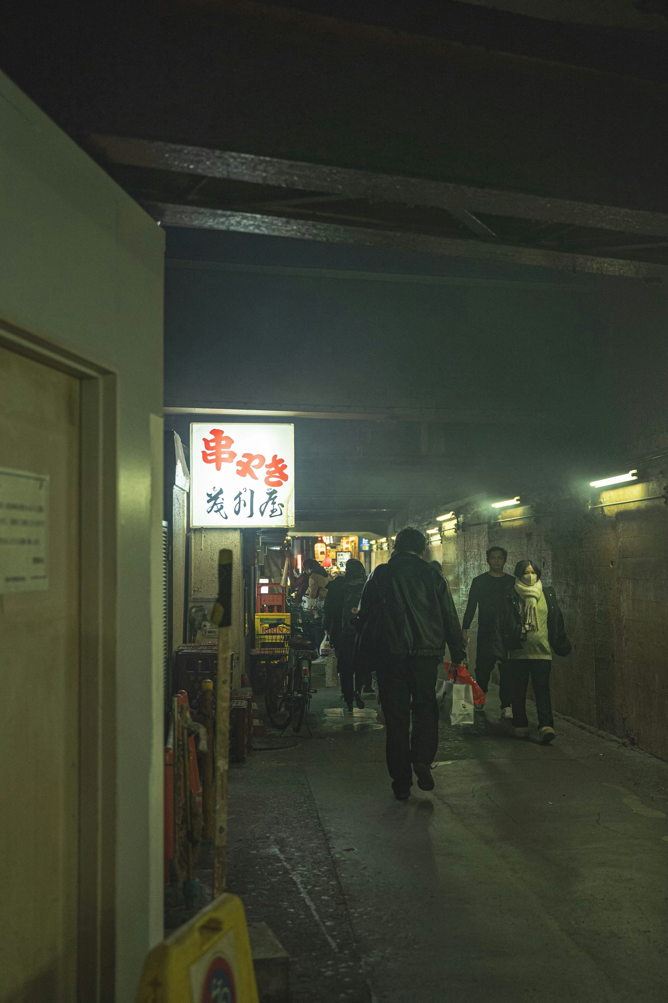 路地の飲食店前で人が行き交う夜の通り