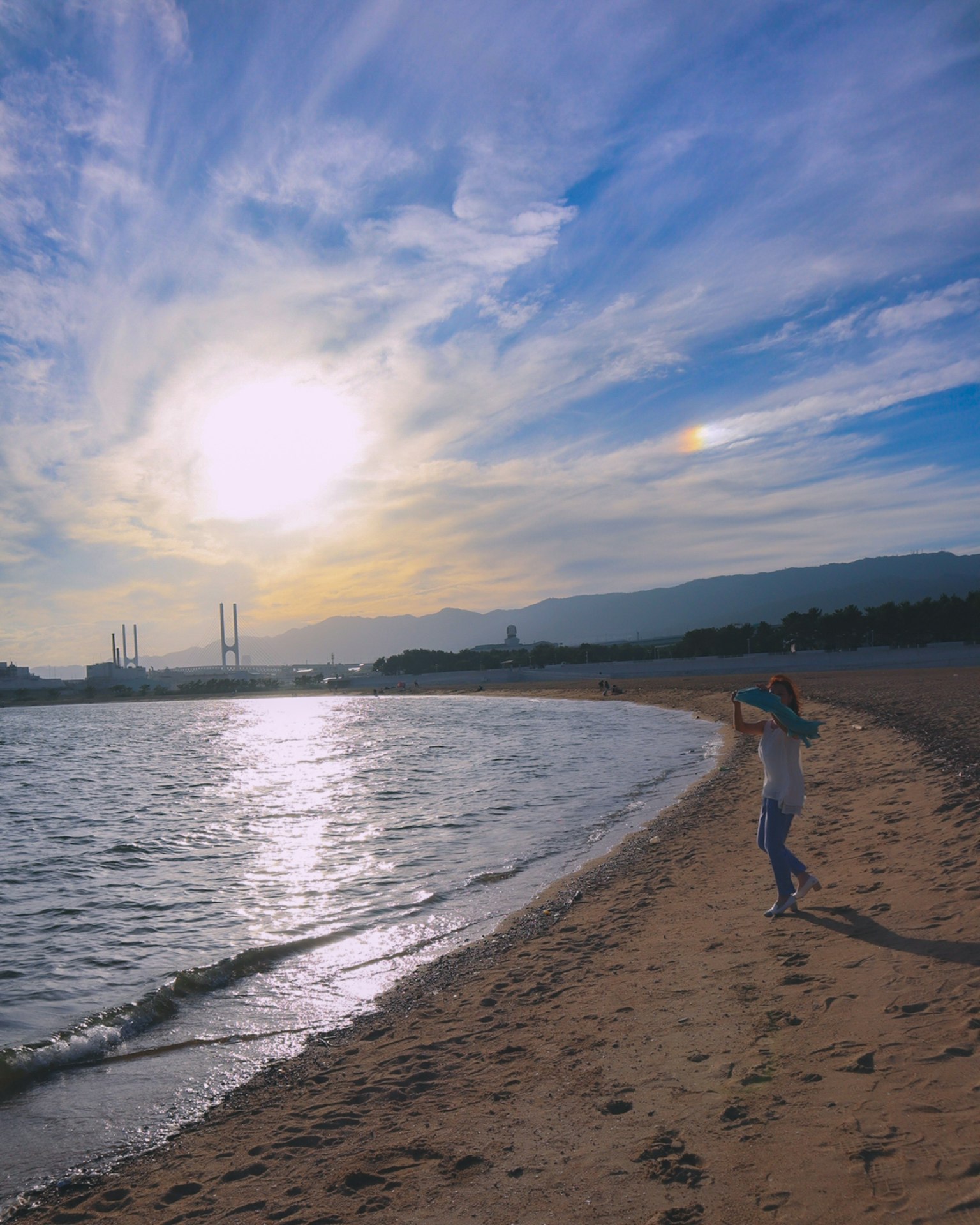 Silhouette di una donna in piedi sulla spiaggia con uno sfondo di tramonto e cielo blu