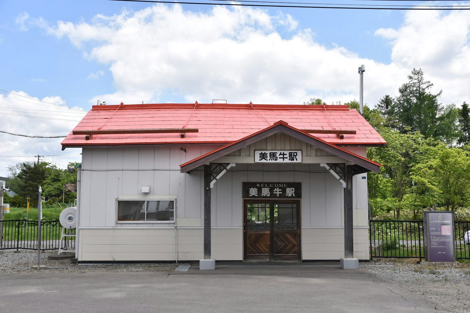 อาคารสถานีรถไฟหลังคาสีแดงและพื้นที่สีเขียวรอบๆ