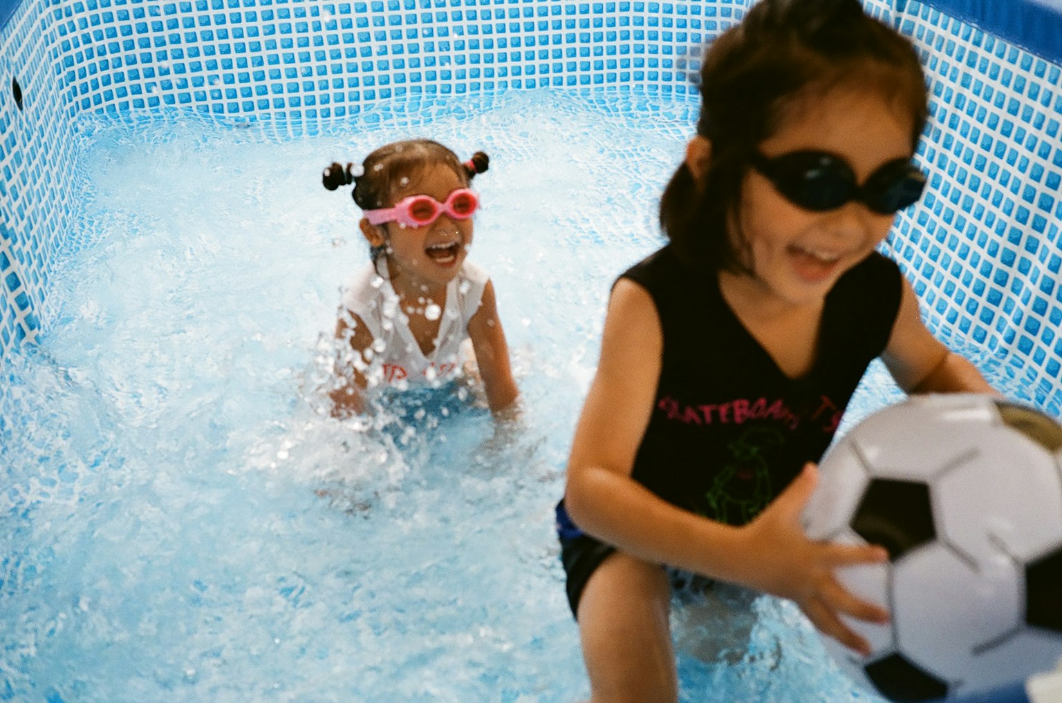 Bambini che giocano in una piscina uno tiene un pallone da calcio e l'altro schizza nell'acqua