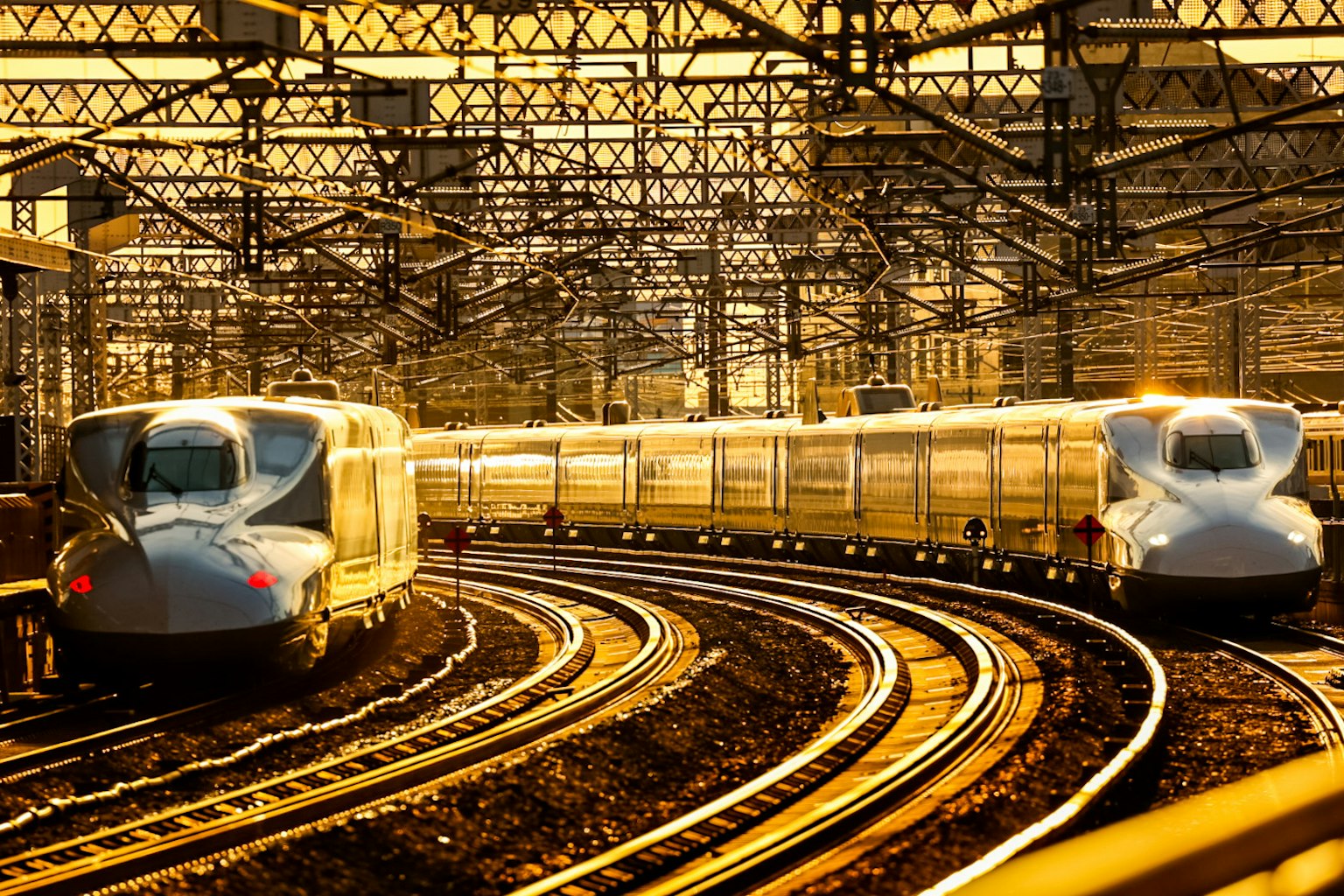 Deux trains Shinkansen se courbent sur des rails au coucher du soleil dans une gare