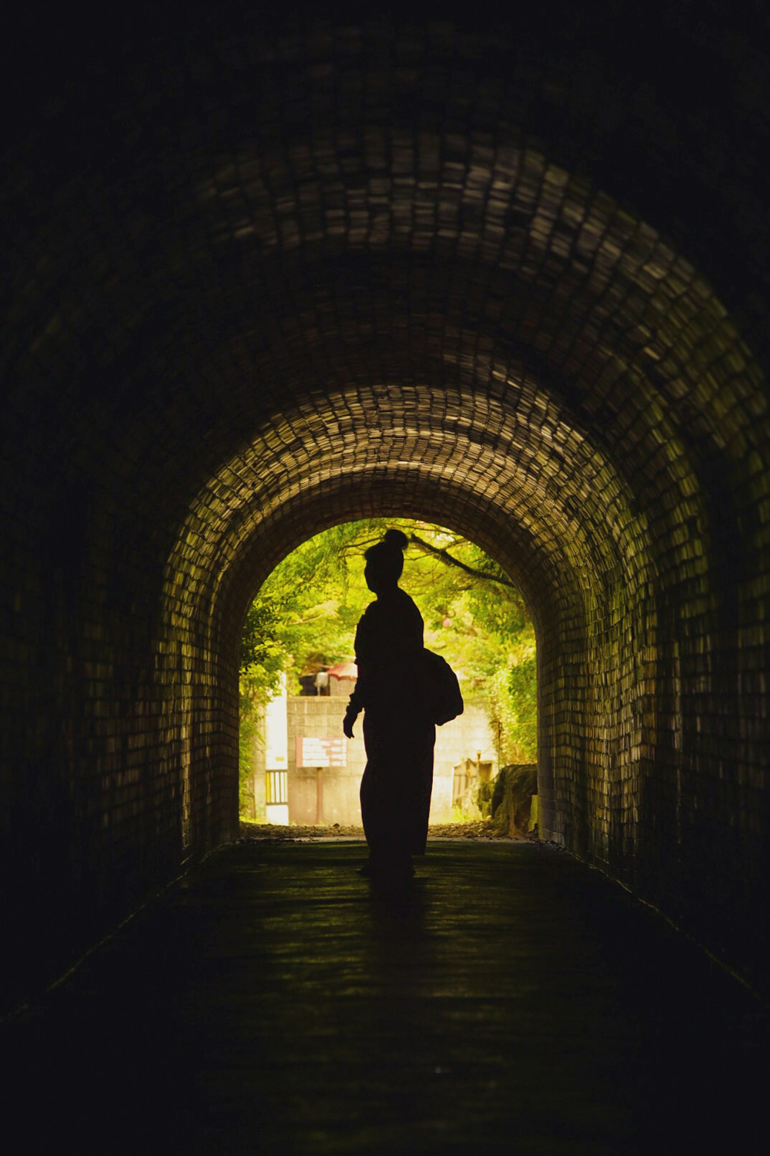 Silhouette einer Person in einem Kimono, die in einem Tunnel mit einem hellen Ausgang steht