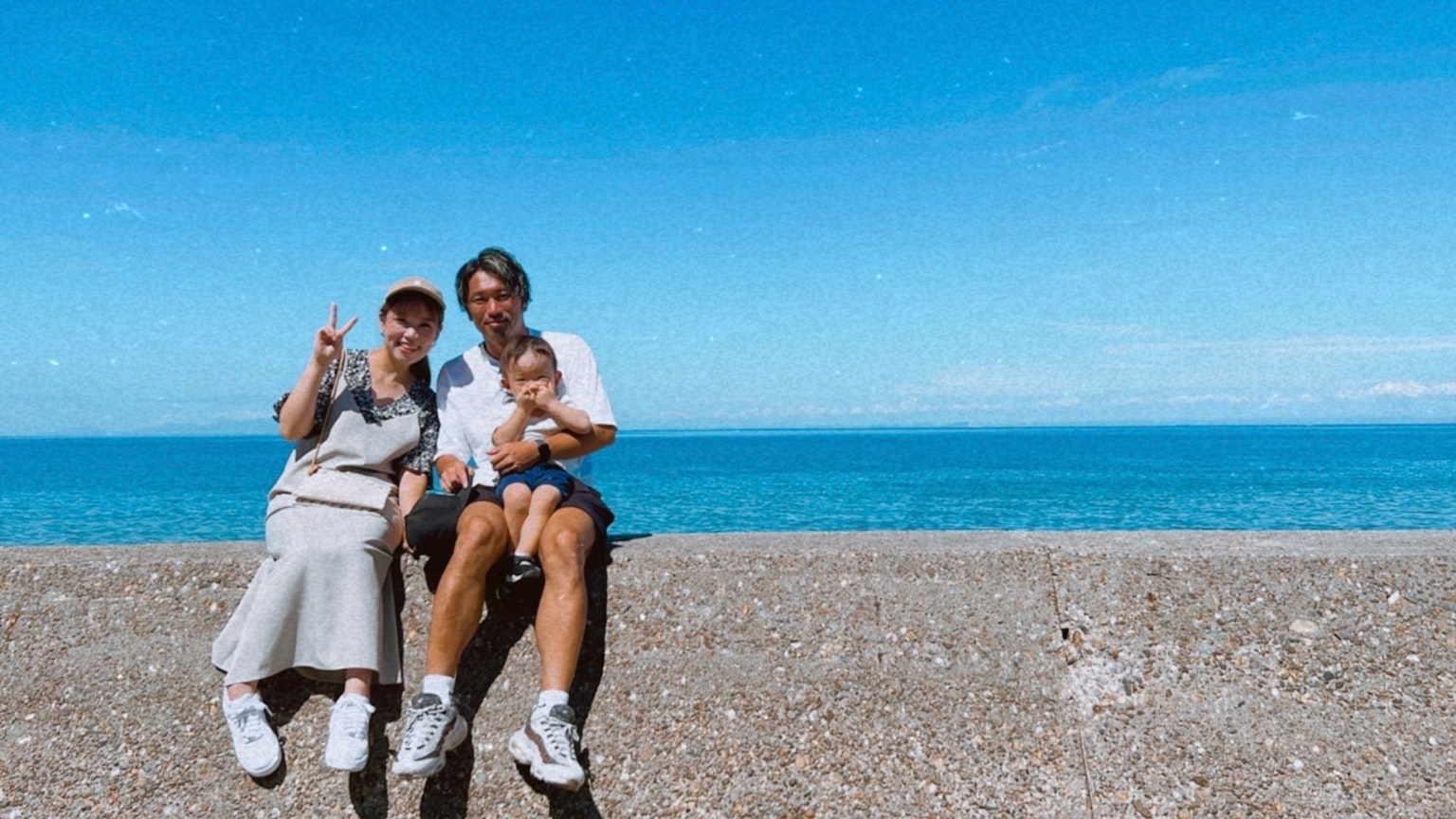 家庭照片，两个微笑的人和一个婴儿坐在蓝色海洋和天空的背景下