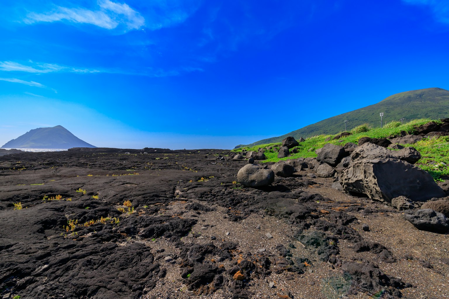 Vue panoramique d'un paysage volcanique avec ciel bleu collines vertes et roches noires