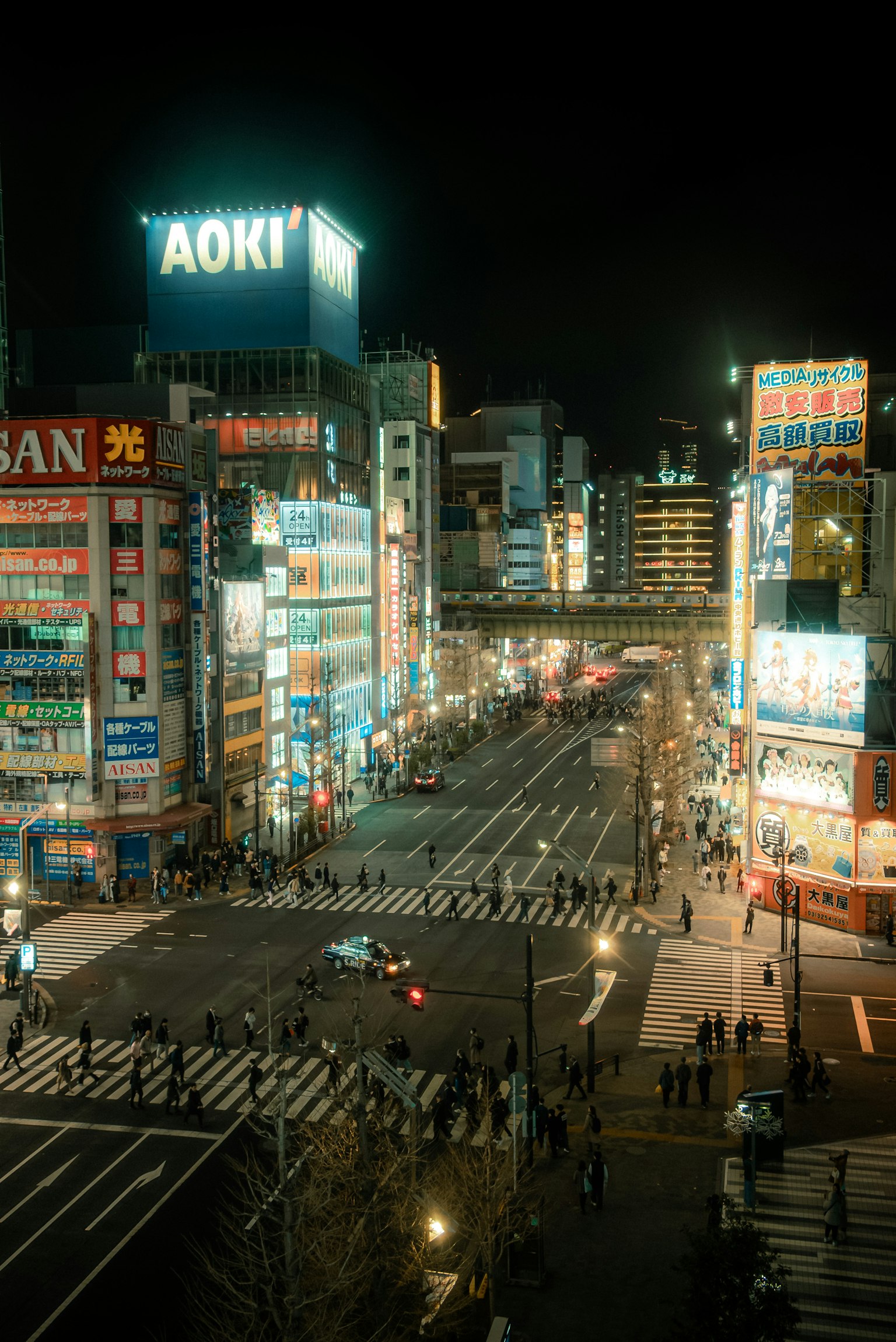 Paysage urbain nocturne avec un panneau AOKI au premier plan d'un carrefour animé
