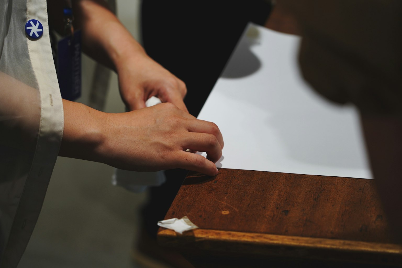 A person's hands handling a piece of paper on a wooden table