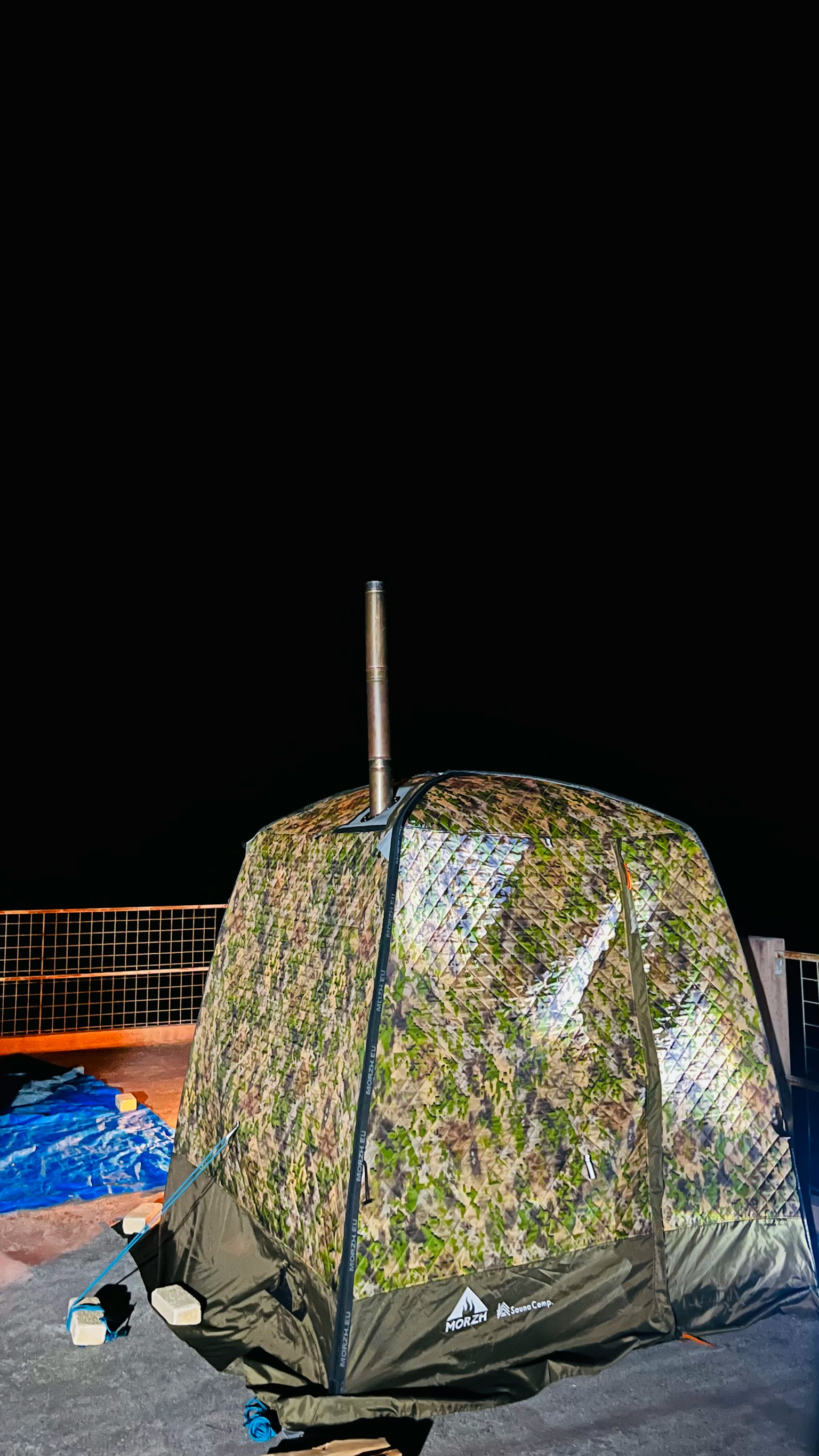 Sebuah tenda kamuflase berdiri di latar belakang hitam