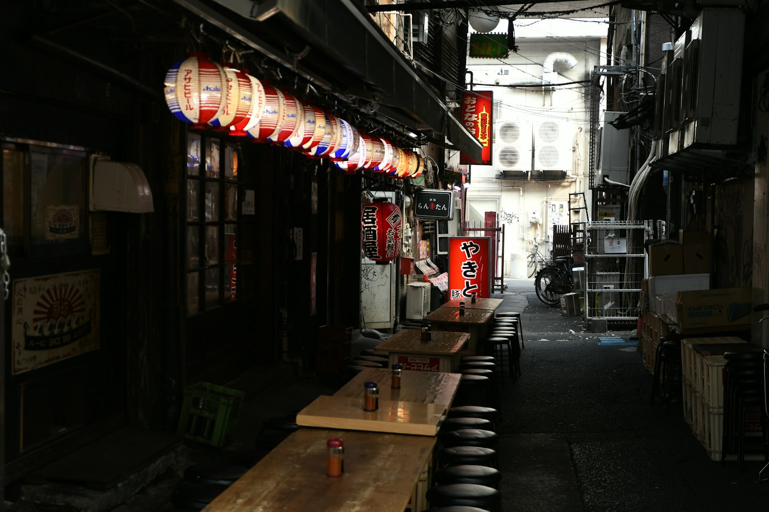 Narrow alley with hanging lanterns and wooden tables in a Japanese izakaya