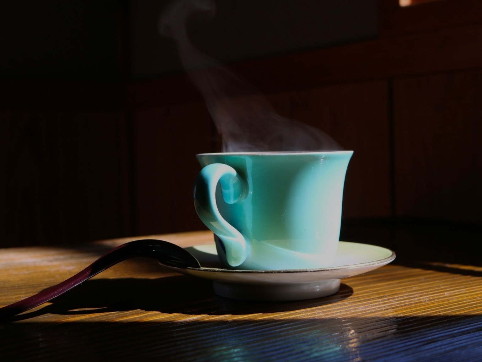 青いカップの湯気の立つコーヒーがテーブルの上に置かれている
