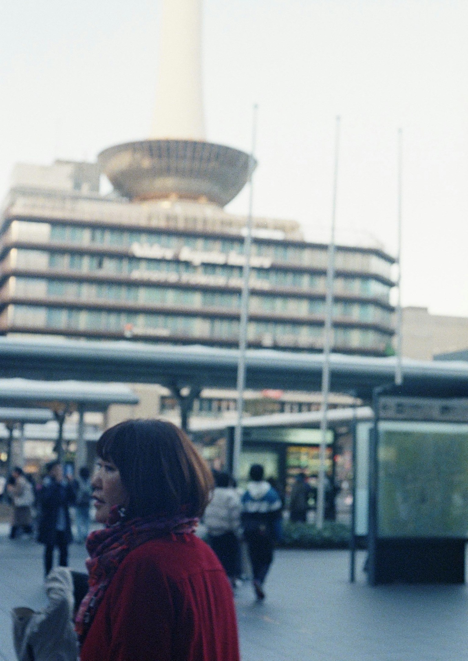 Una mujer con un abrigo rojo caminando en una plaza de la ciudad con un edificio moderno al fondo