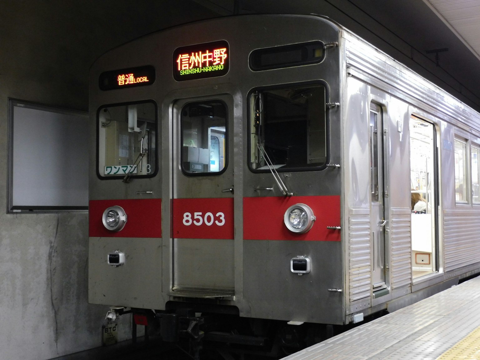 Train argenté avec une bande rouge stationné à une gare