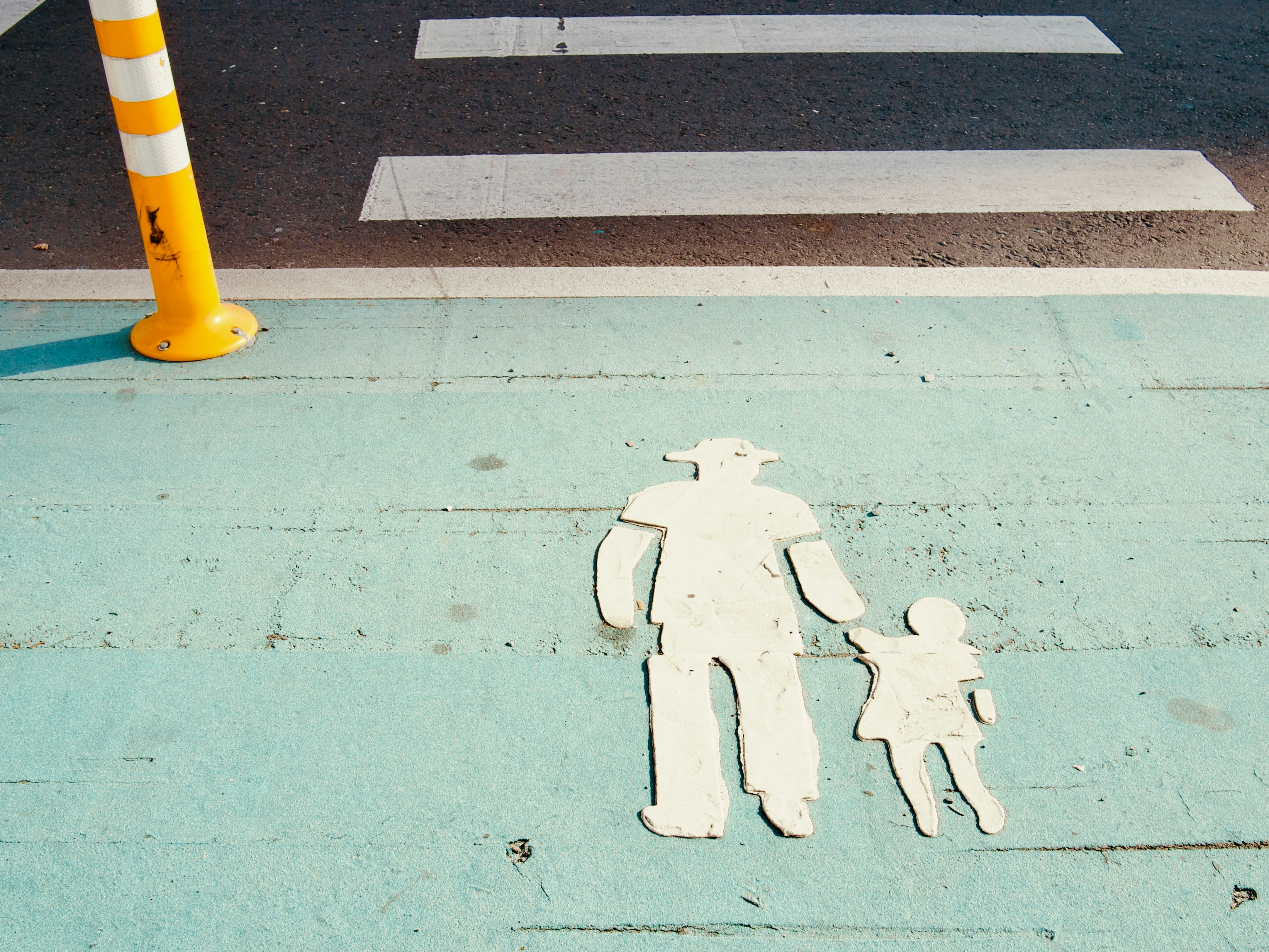 青い歩道に描かれた人と子供のシルエットと交通コーン