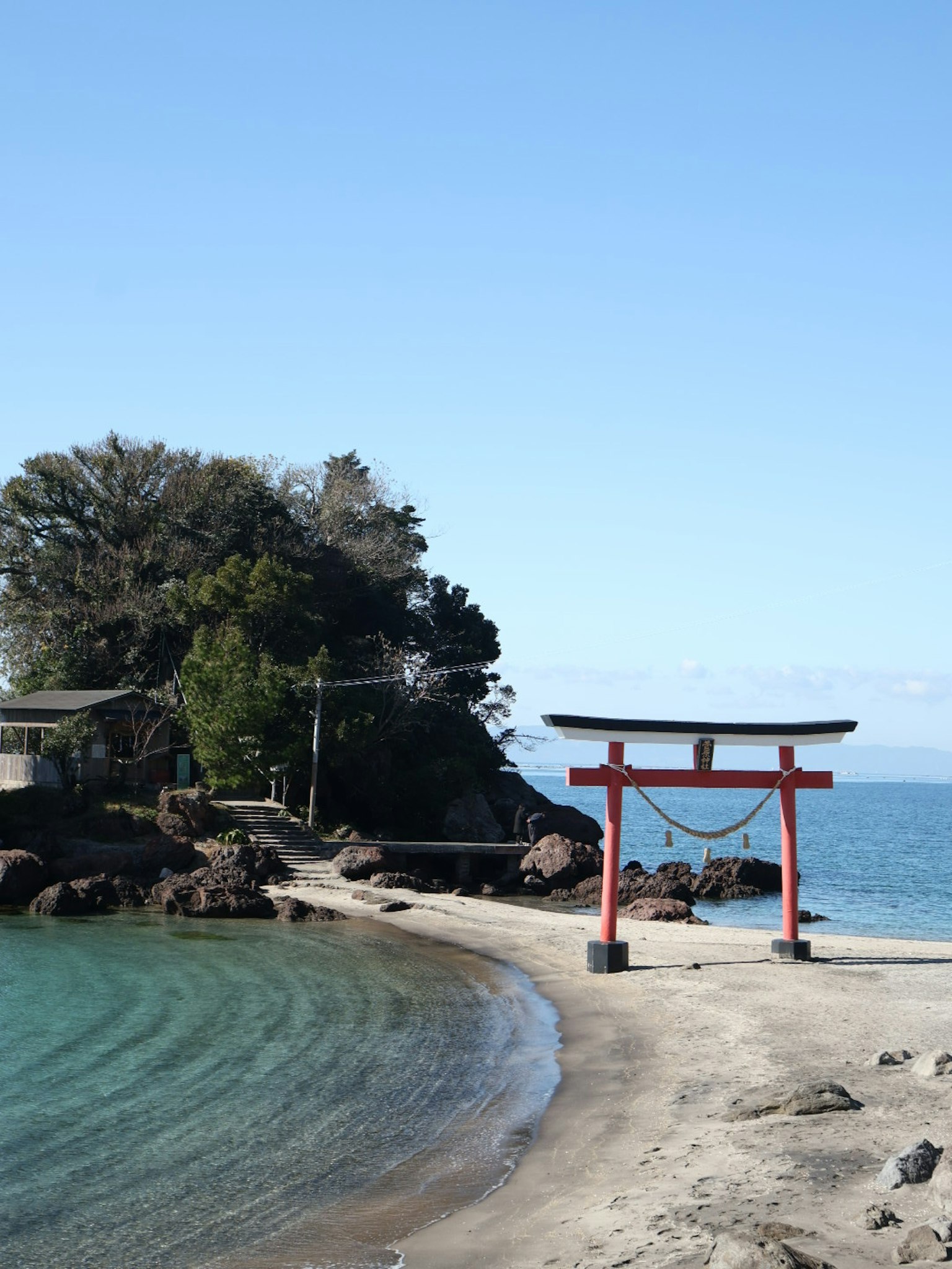 Vista panoramica di un torii rosso accanto al mare blu calmo e alla spiaggia