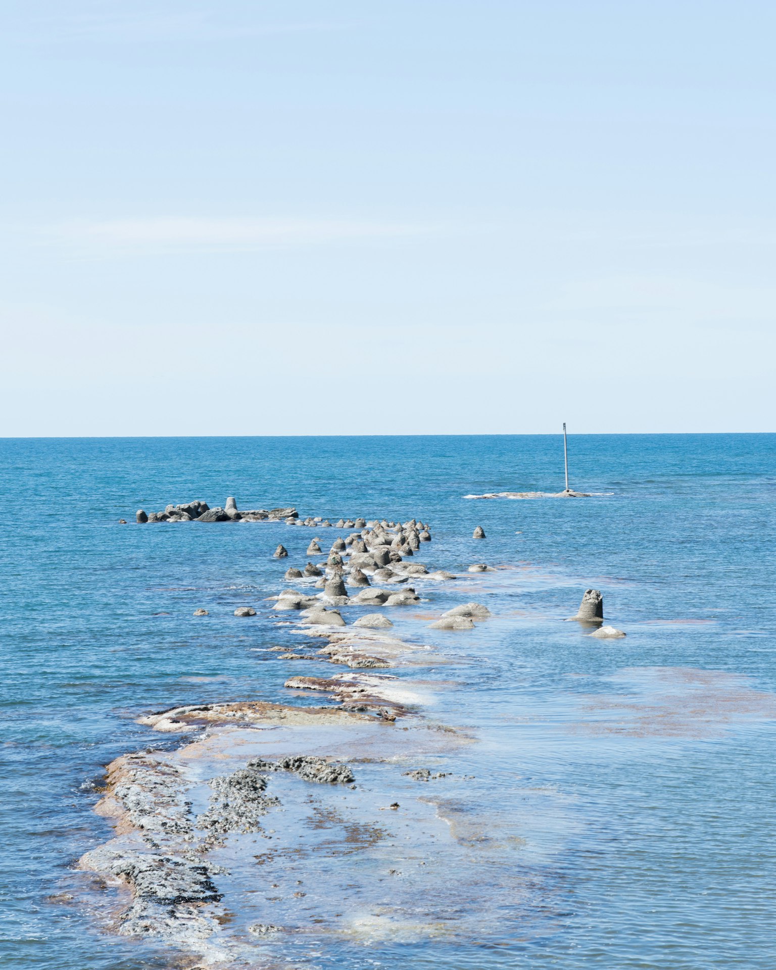 Rock pathway in blue sea under clear sky