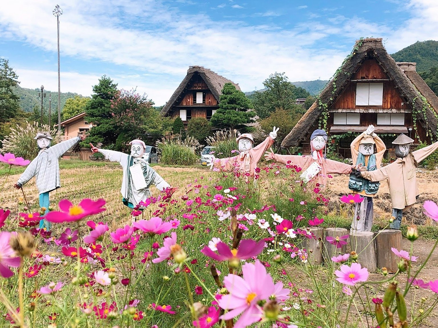 Vista panoramica di case tradizionali con tetti in paglia e figure che posano tra fiori colorati
