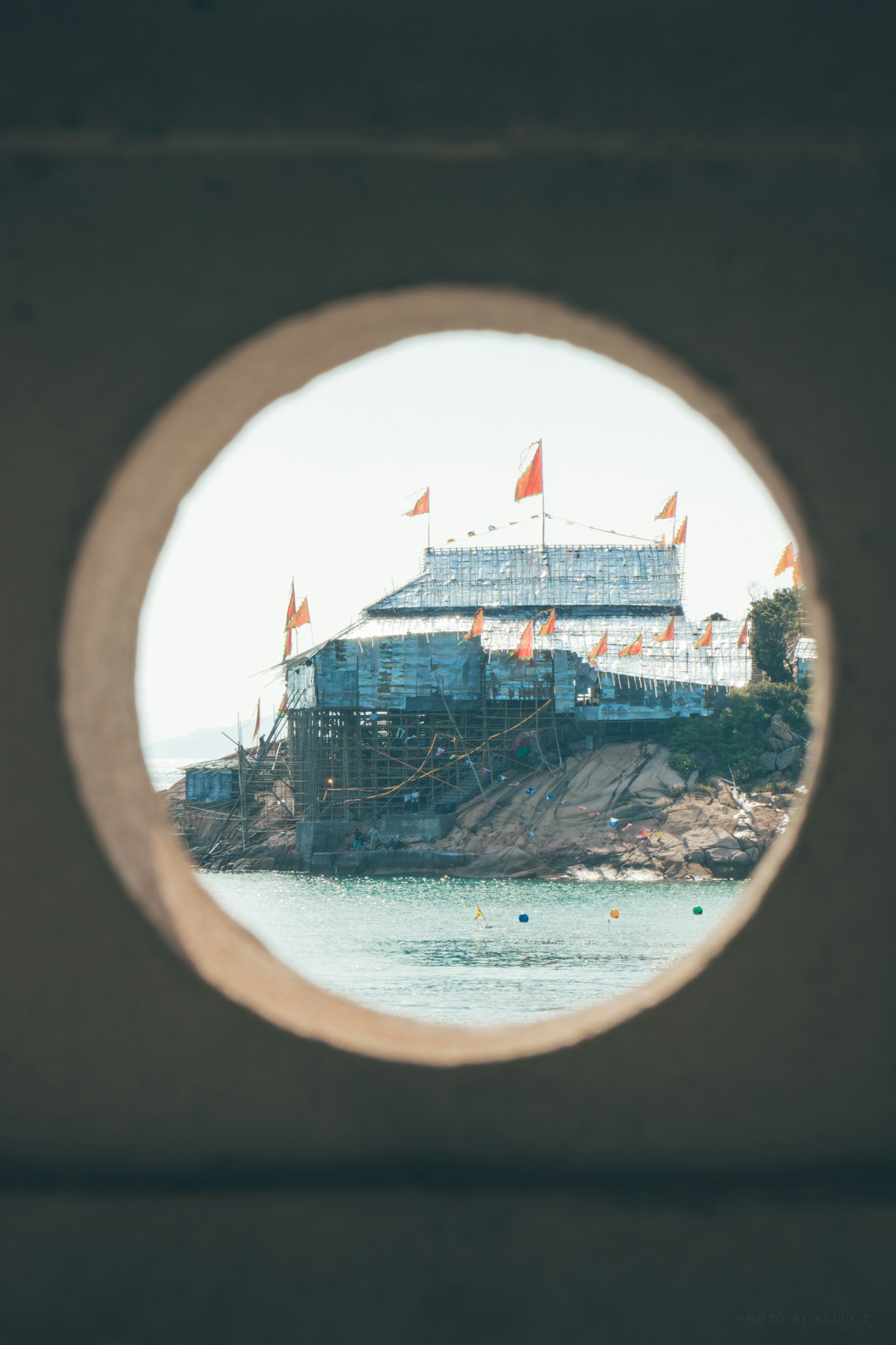 kreisförmiger Blick durch eine Öffnung auf eine Festbühne am Meer (Tin-Hau-Festival der Insel Po Toi)