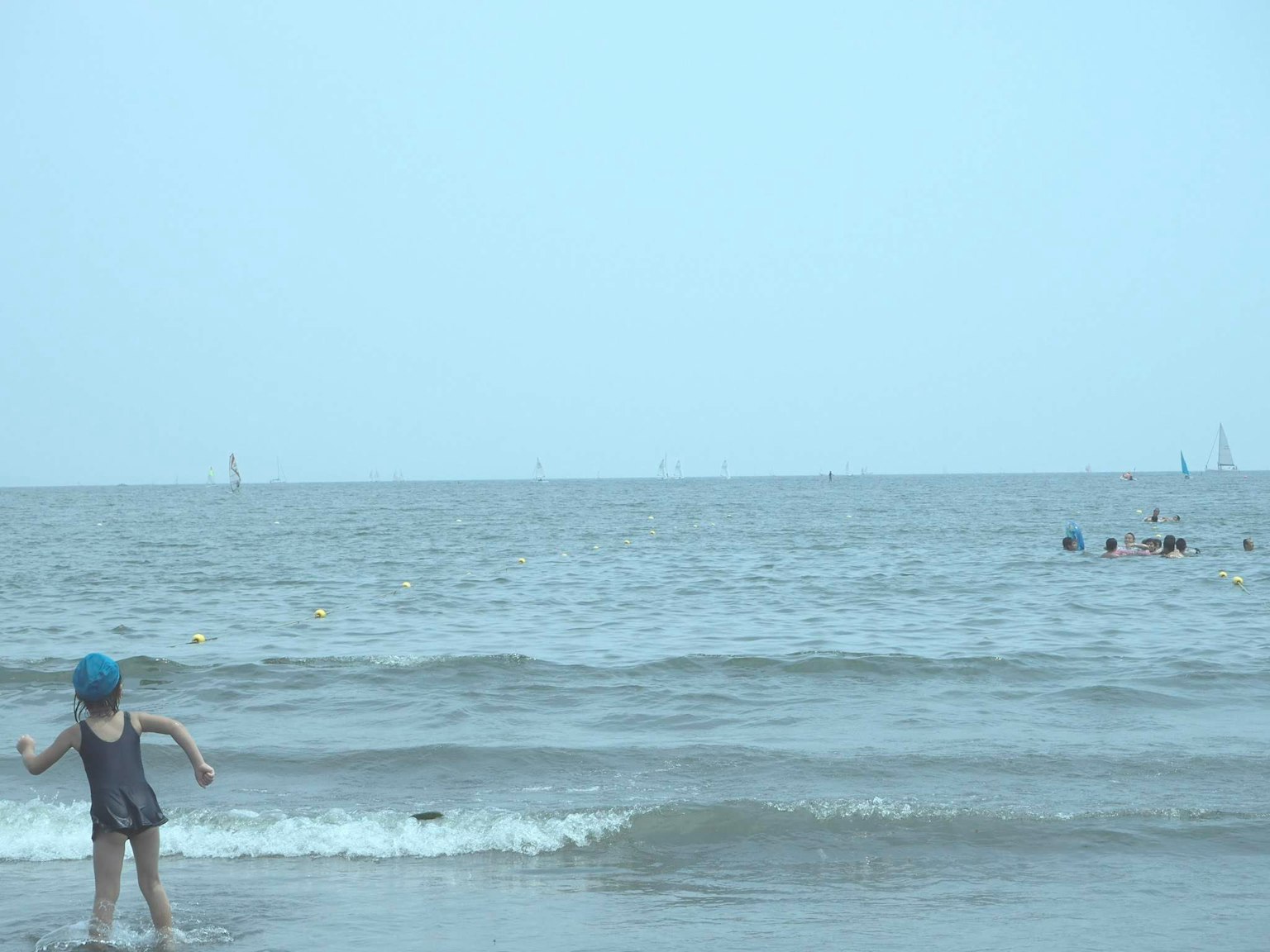 Anak yang mengenakan topi biru bermain di pantai