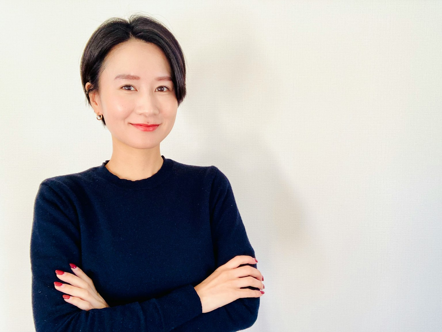 女性微笑著，雙臂交叉，站在白色背景前