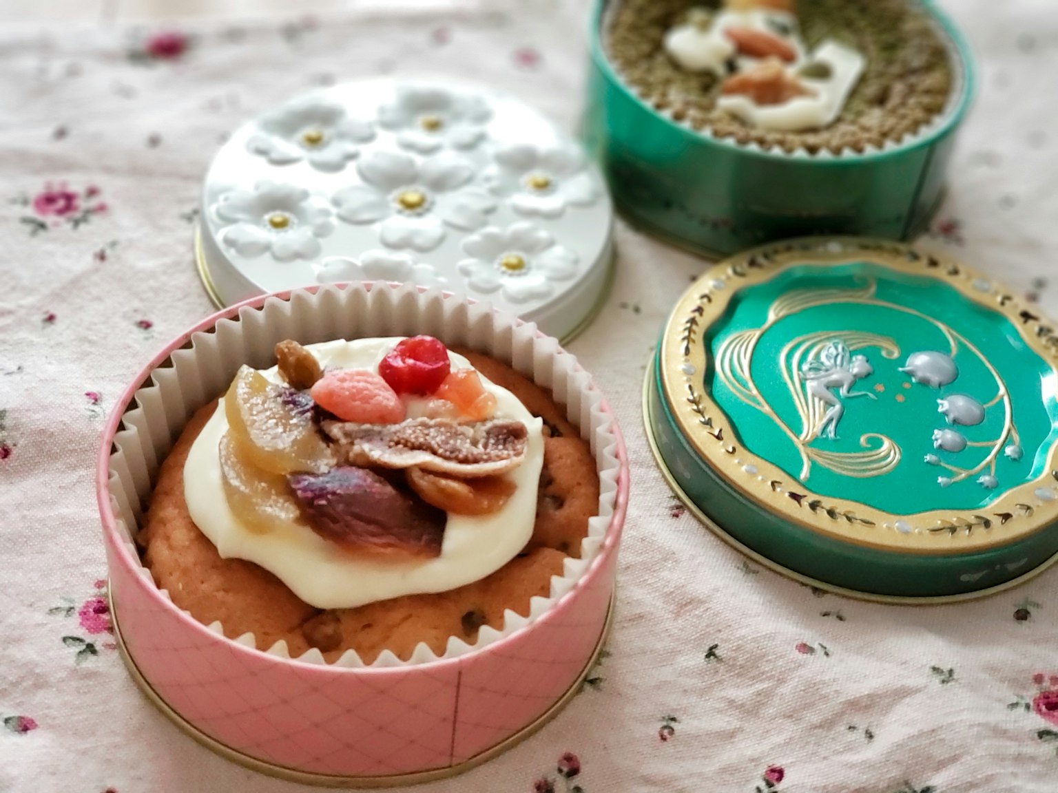 Verschiedene Kuchen in dekorativen Dosen auf einem blumigen Tischdecken