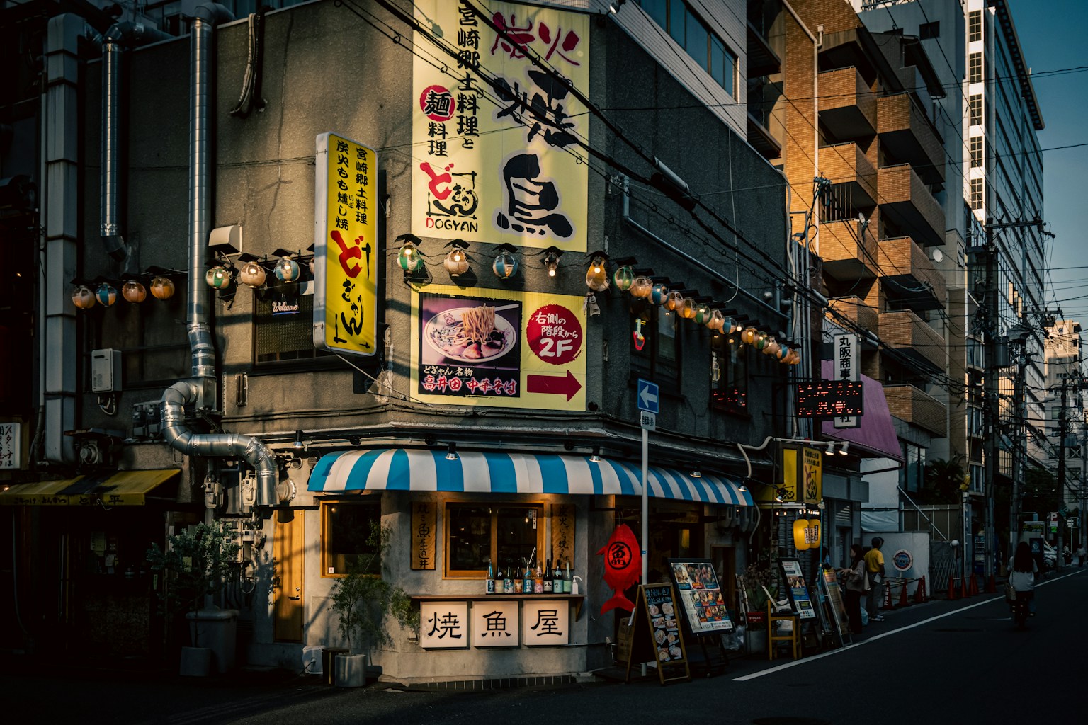 Lebhaftes Restaurant an einer Straßenecke in Japan mit hellen Schildern und Laternen
