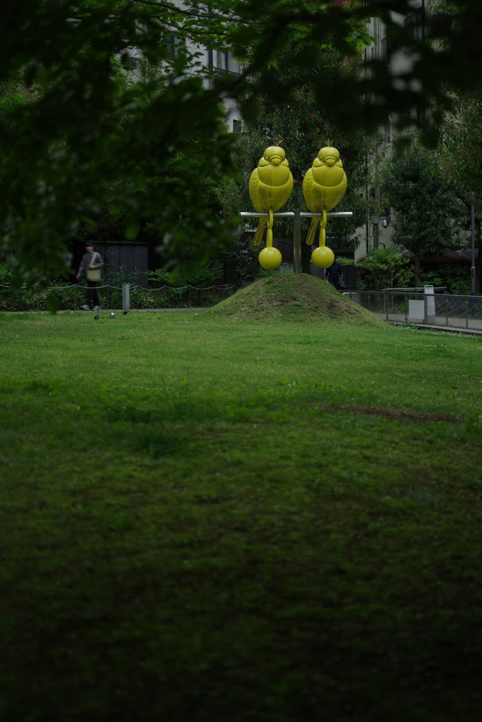 Zwei gelbe Vogel-Skulpturen stehen auf einer grasbewachsenen Fläche