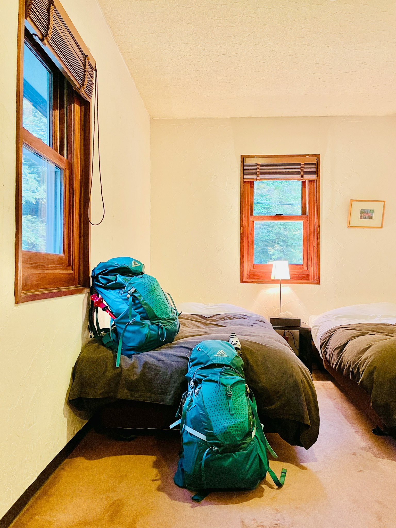 Sebuah kamar sederhana dengan dua ransel hijau di samping dua tempat tidur