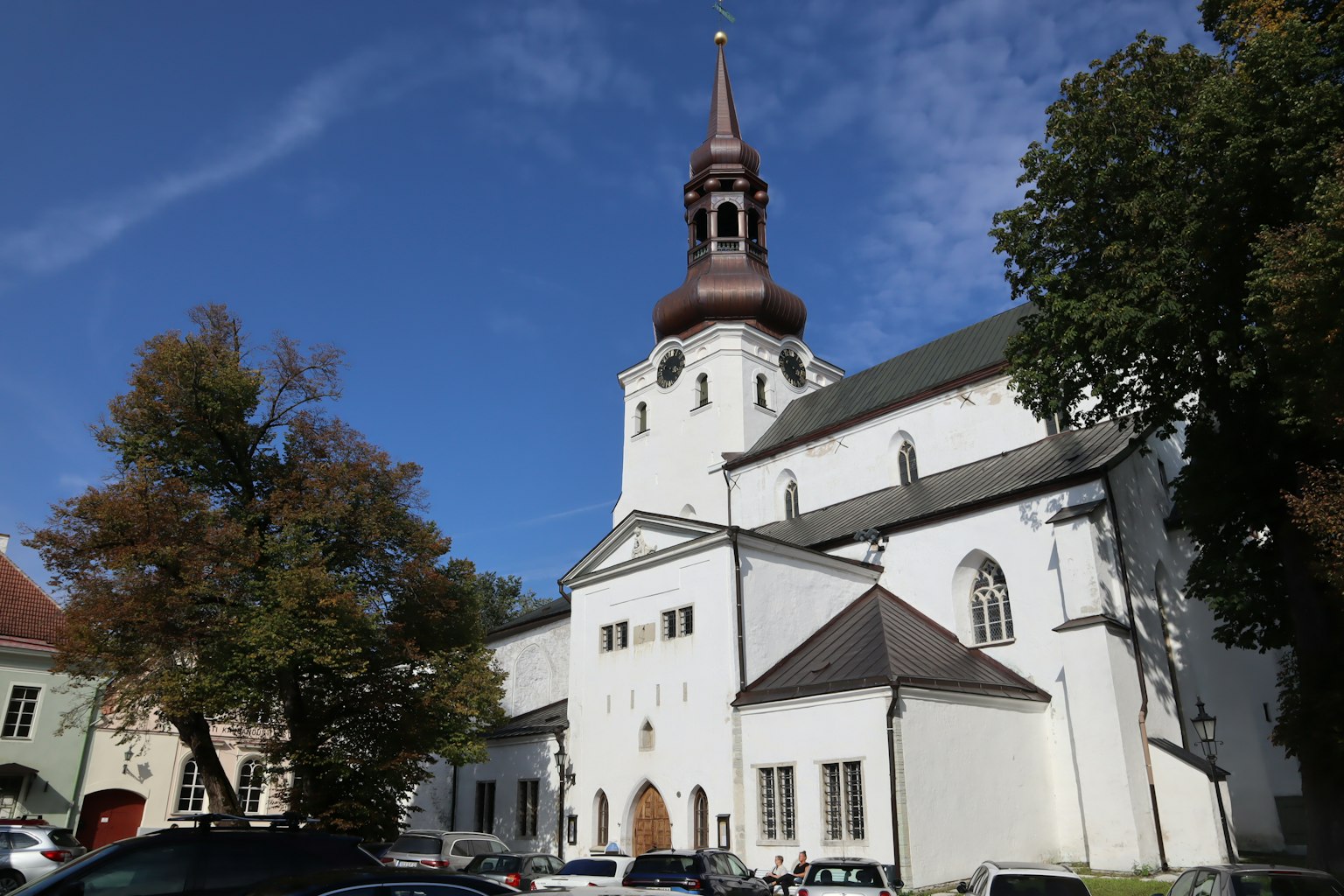 Église blanche avec une tour brune entourée d'arbres verts et d'un ciel bleu
