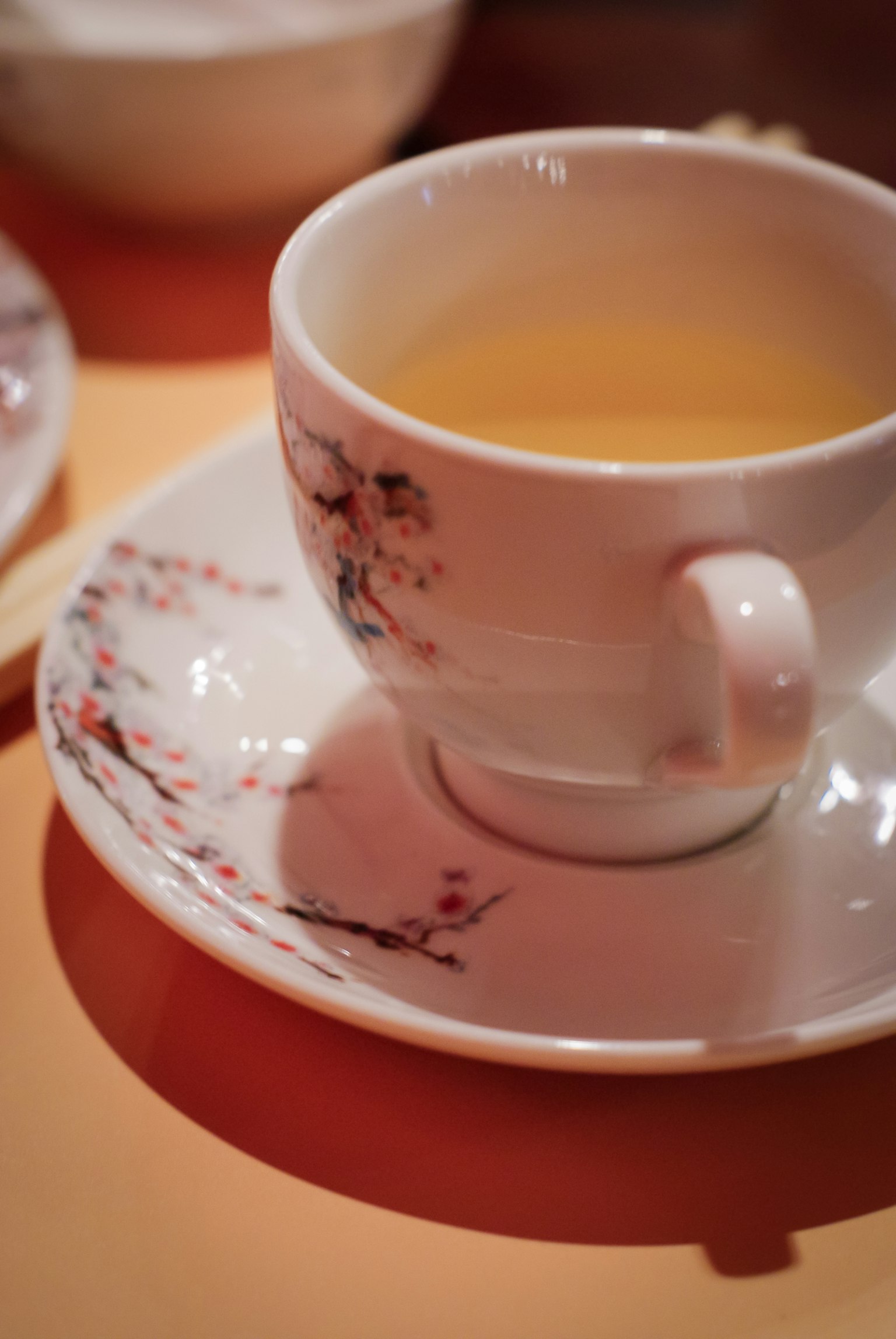 一只带有美丽樱花图案的茶杯，盛满黄色茶，放在匹配的茶托上