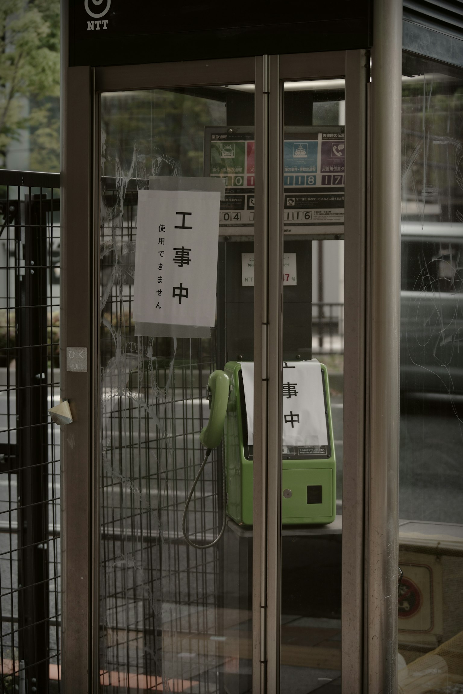 Image of a phone booth under construction Sign indicating construction on the window Green phone inside and surrounding scenery