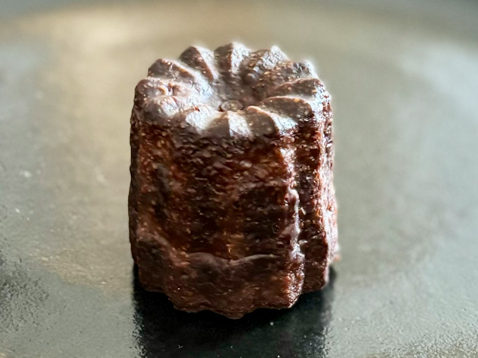 Un canelé magnifiquement formé posé sur une assiette noire