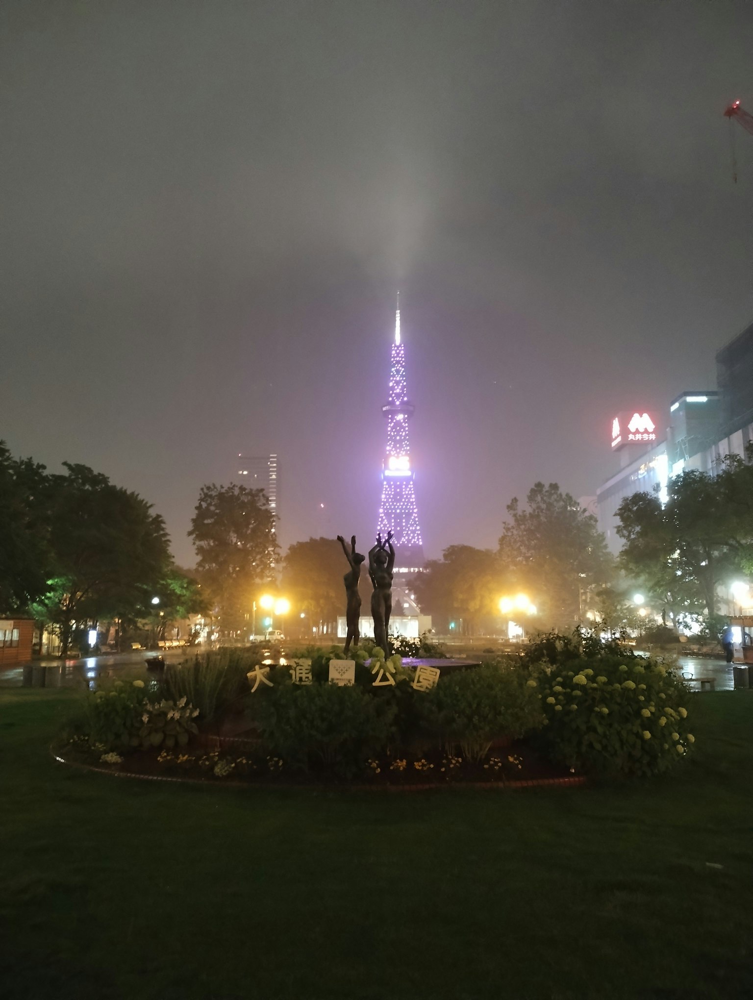 Scène de parc avec une tour violette enveloppée de brouillard et des lumières environnantes avec une statue centrale