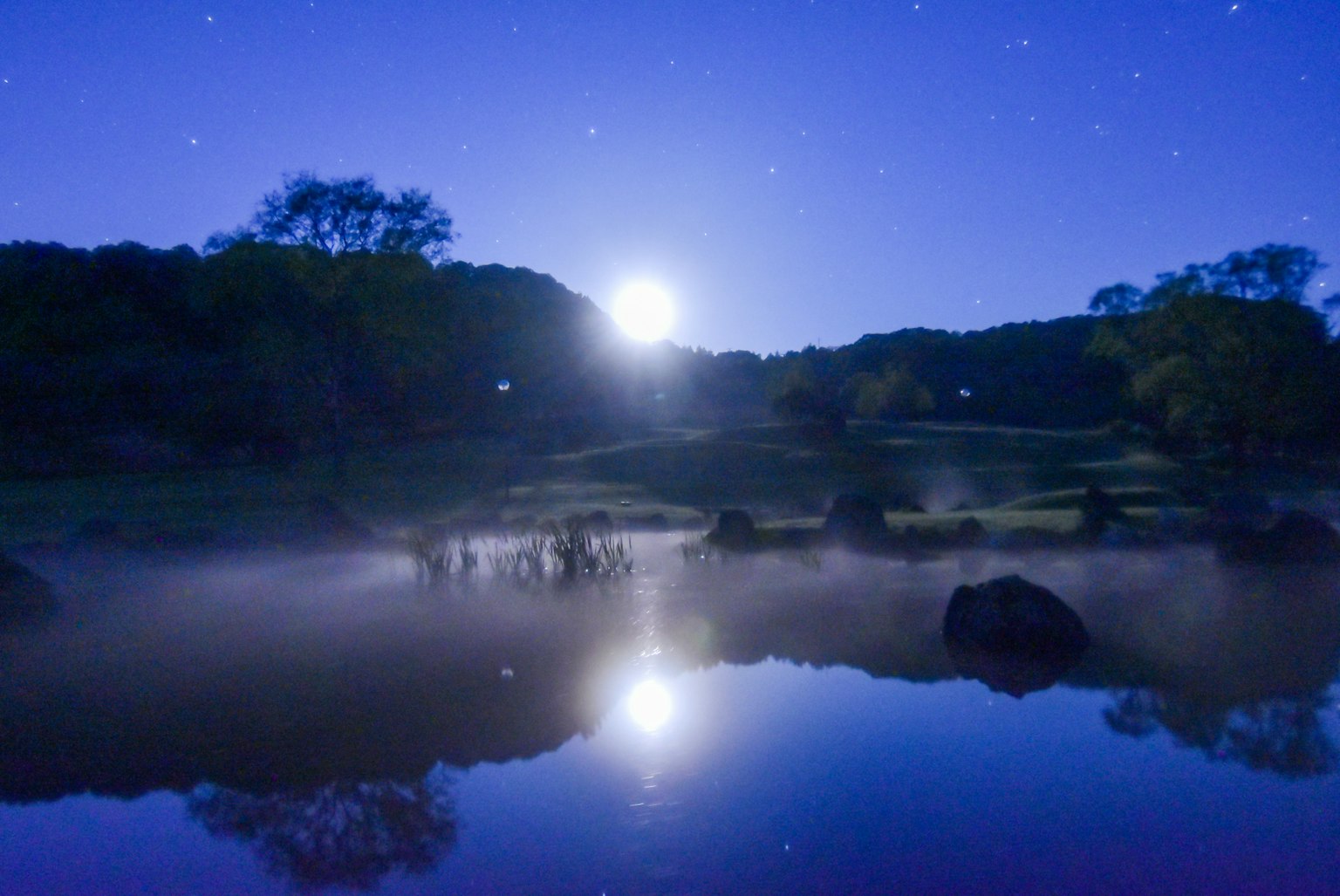 Serene lake landscape illuminated by moonlight with stars in the night sky and mist on the water