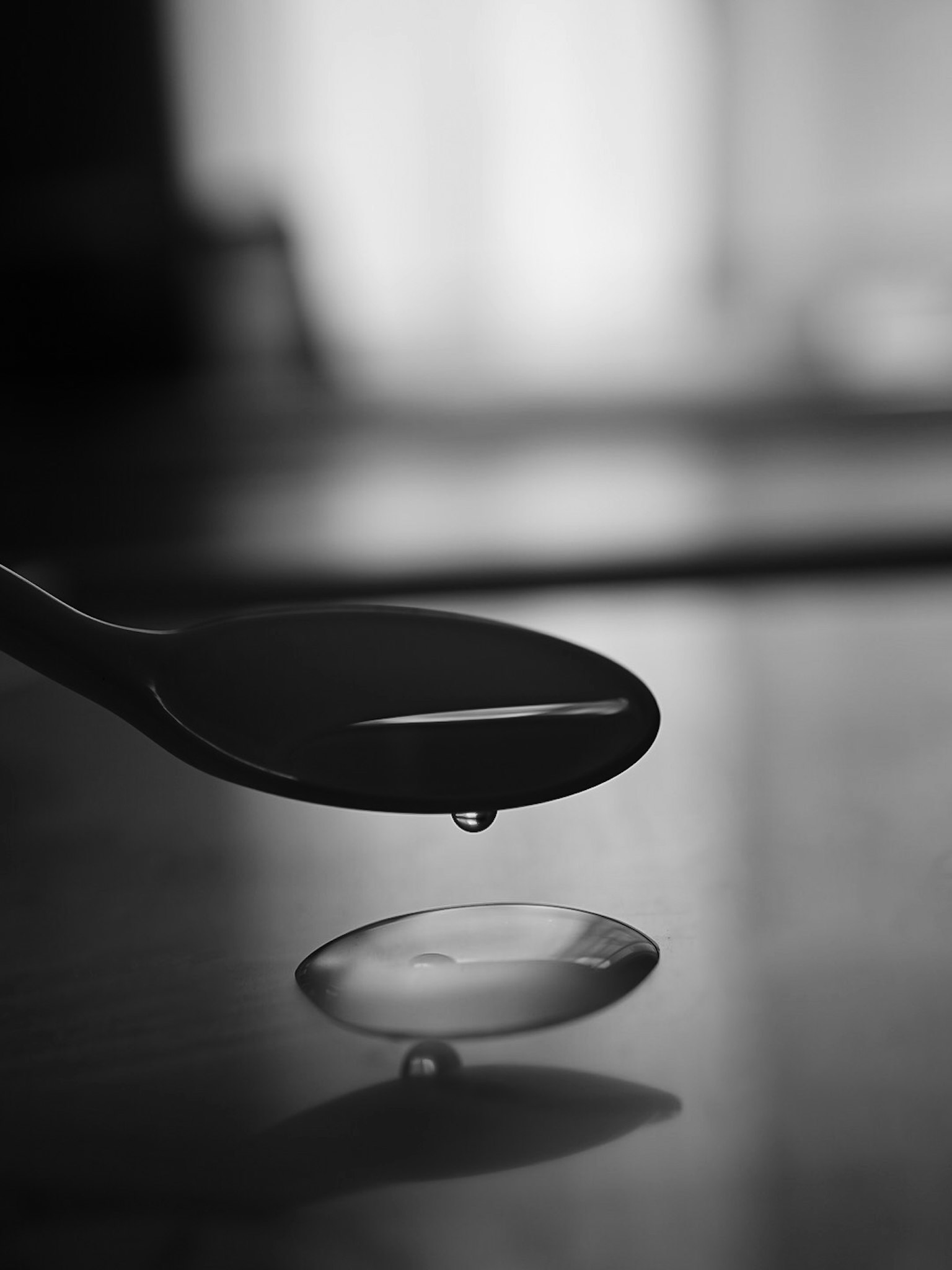 Black spoon with a droplet of water falling from its tip in monochrome