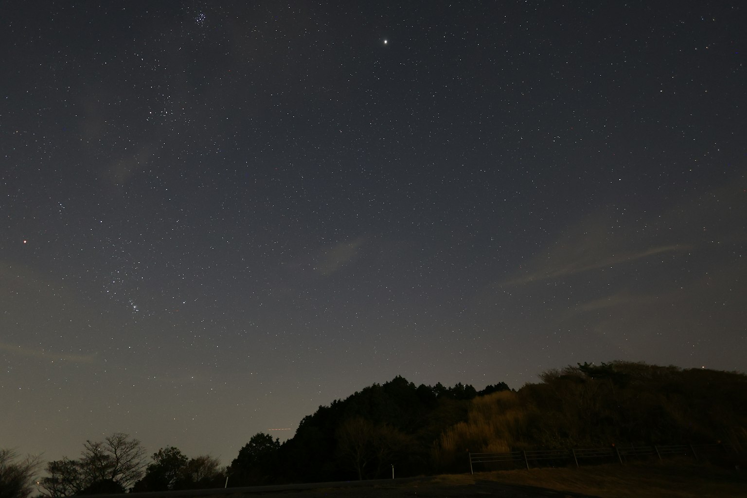 Starry night sky featuring bright stars and a silhouette of a mountain