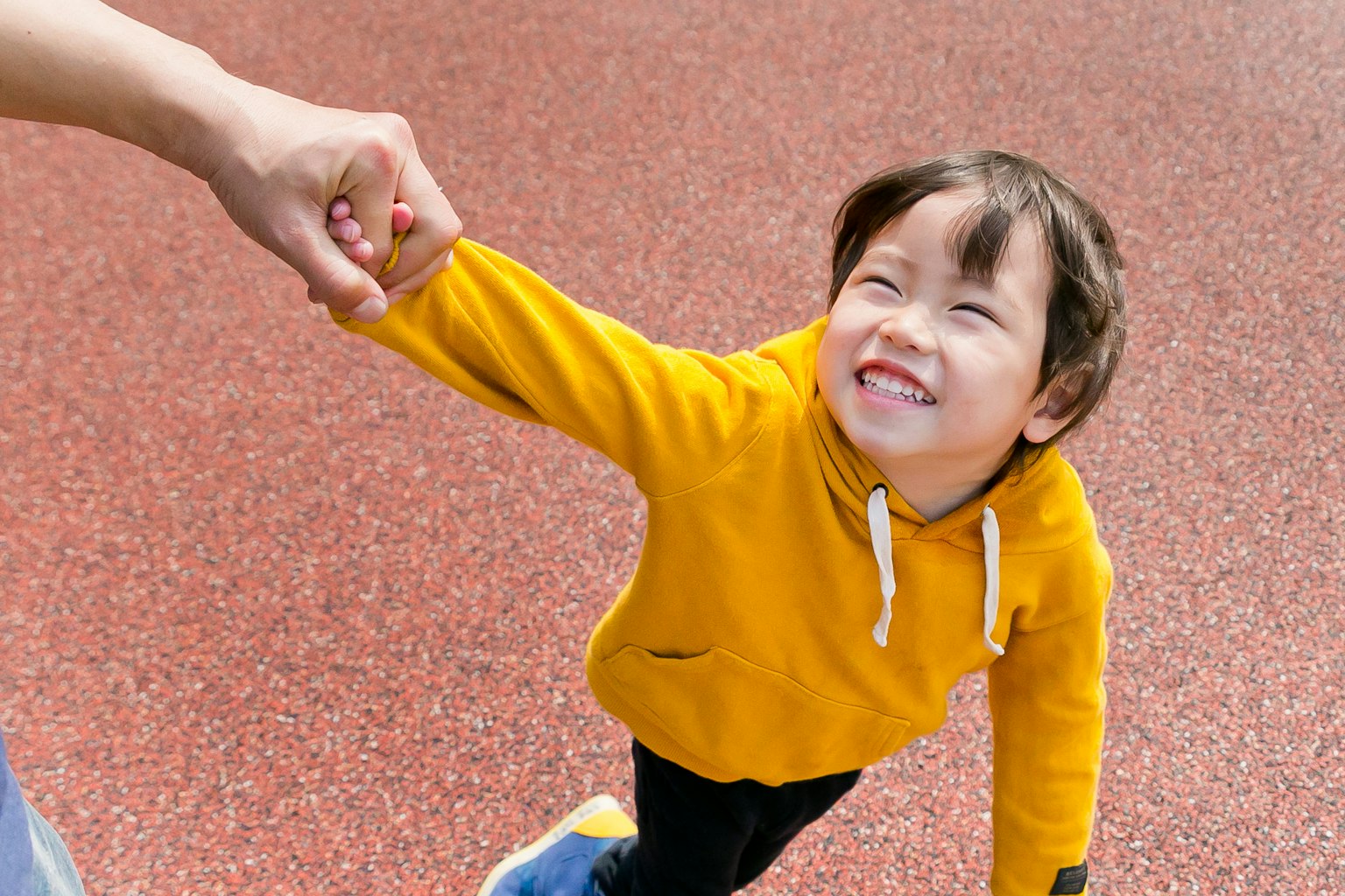Anak dengan hoodie kuning tersenyum saat ditarik oleh tangan orang dewasa