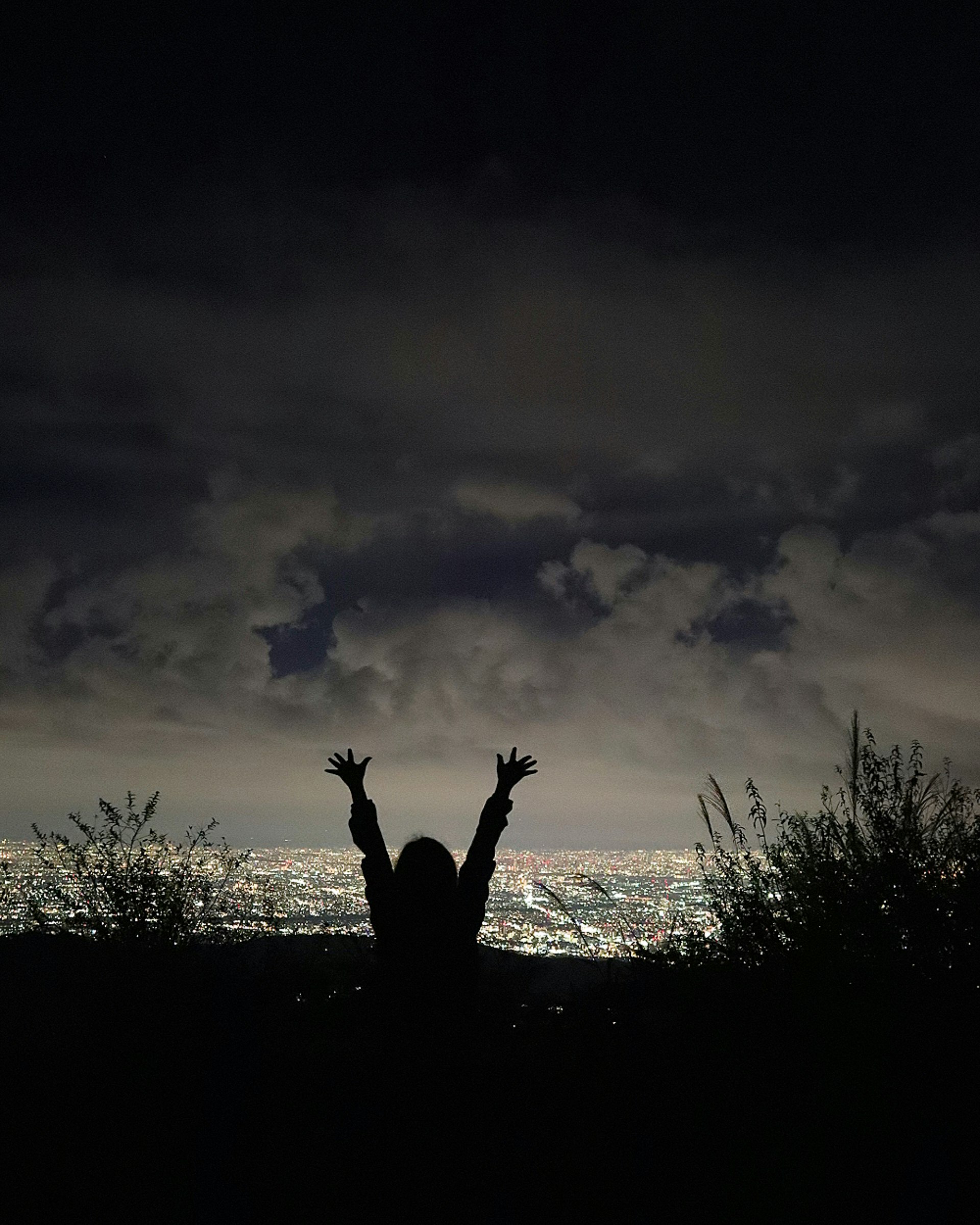 六甲山からの夜景を見上げるシルエットの人物と雲の空