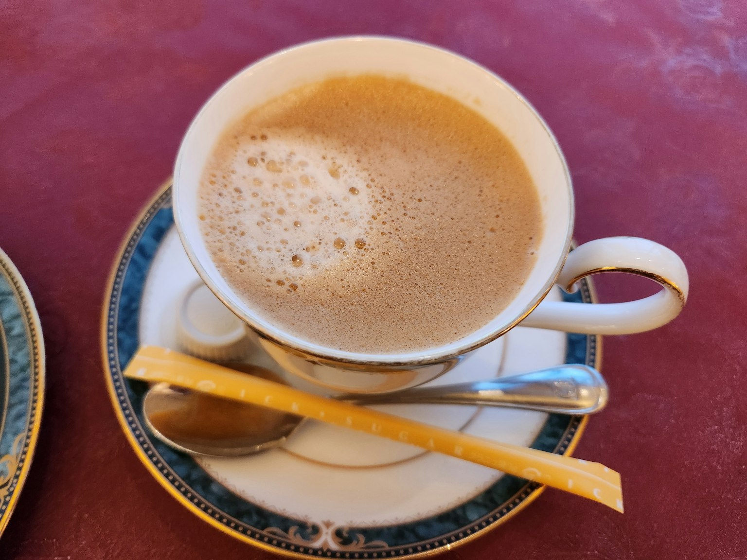 ถ้วยกาแฟที่มีฟองอยู่บนจานตกแต่งและช้อน