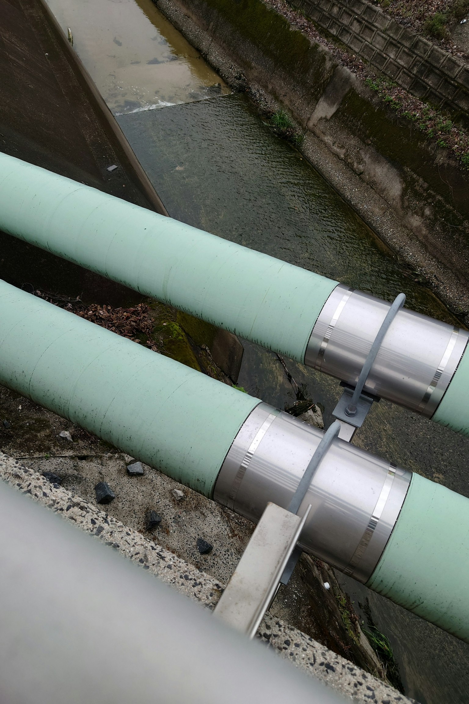 Tuberías verdes aseguradas con abrazaderas metálicas sobre un canal de agua estrecho