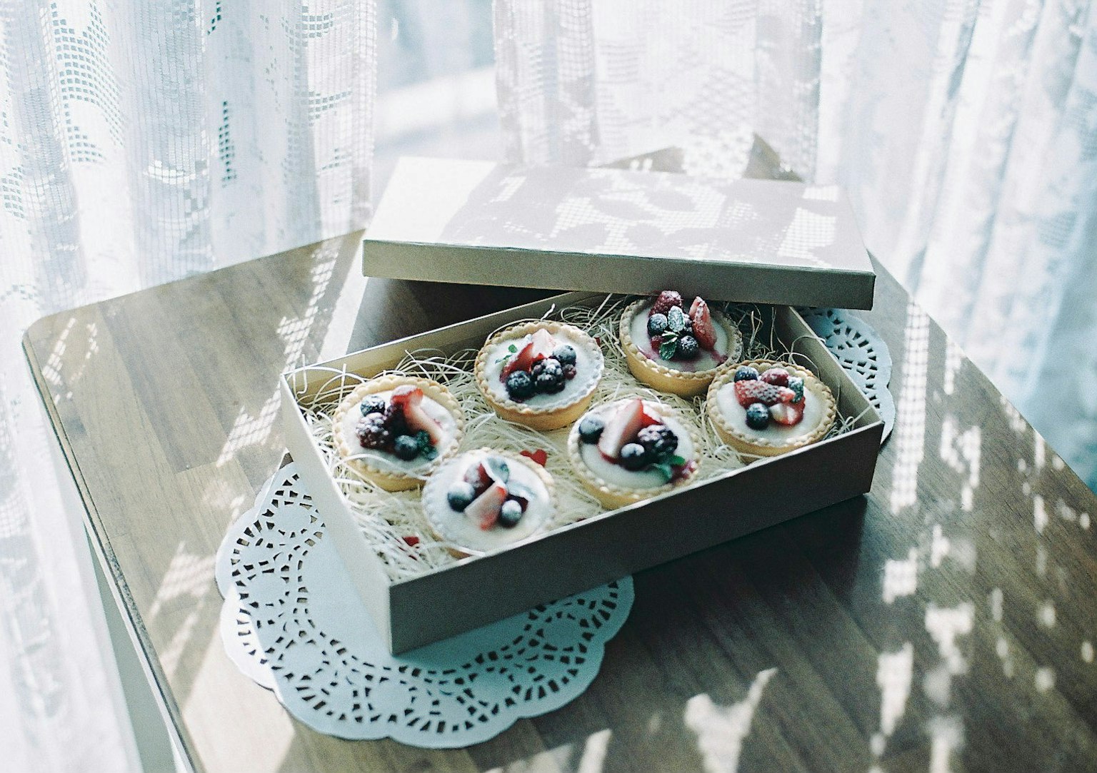 Tartas de frutas coloridas dispuestas en una pequeña caja con un delicado camino de encaje bajo una luz suave
