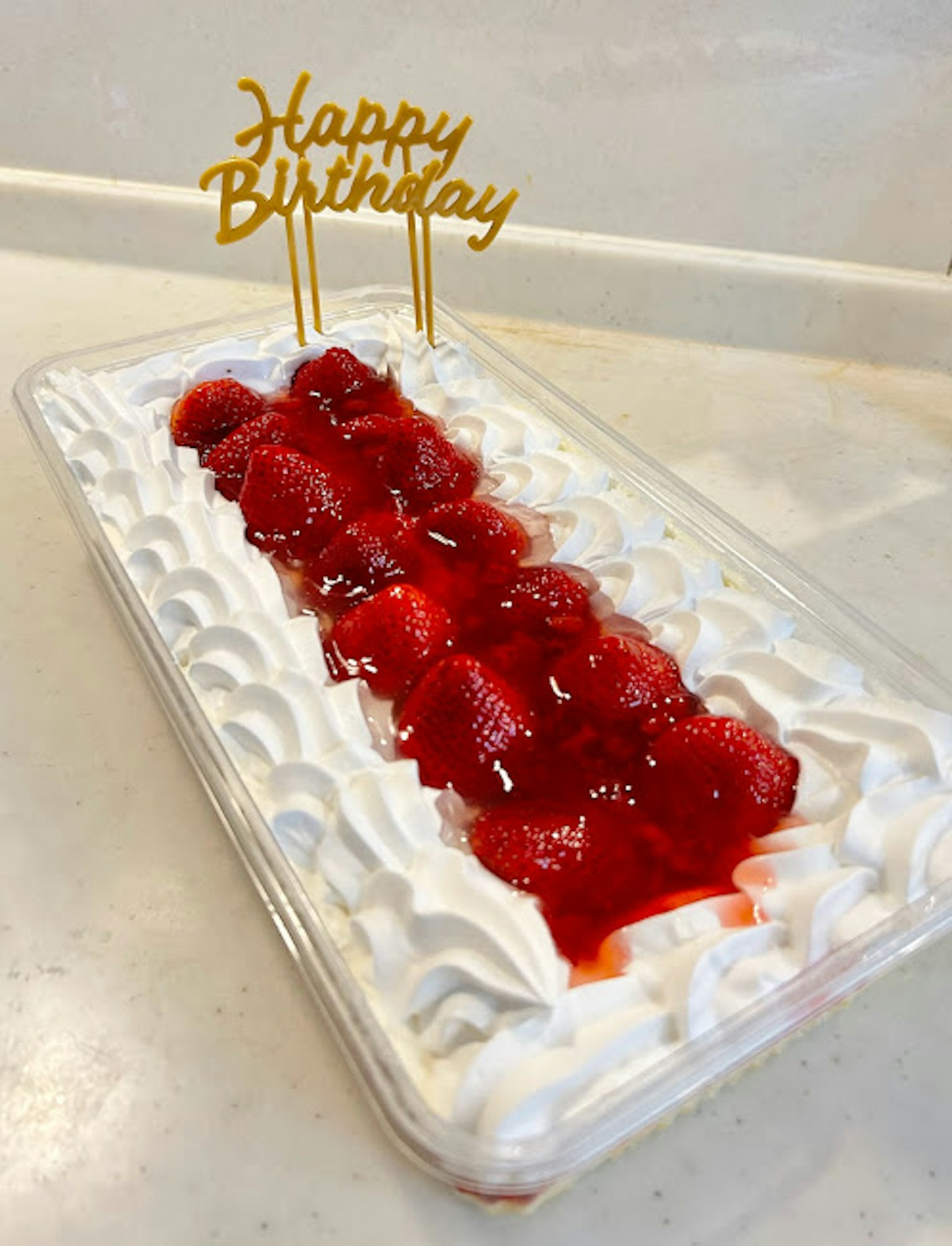 빨간 잼과 휘핑크림이 얹힌 생일 케이크에 금색 Happy Birthday 토퍼가 있습니다