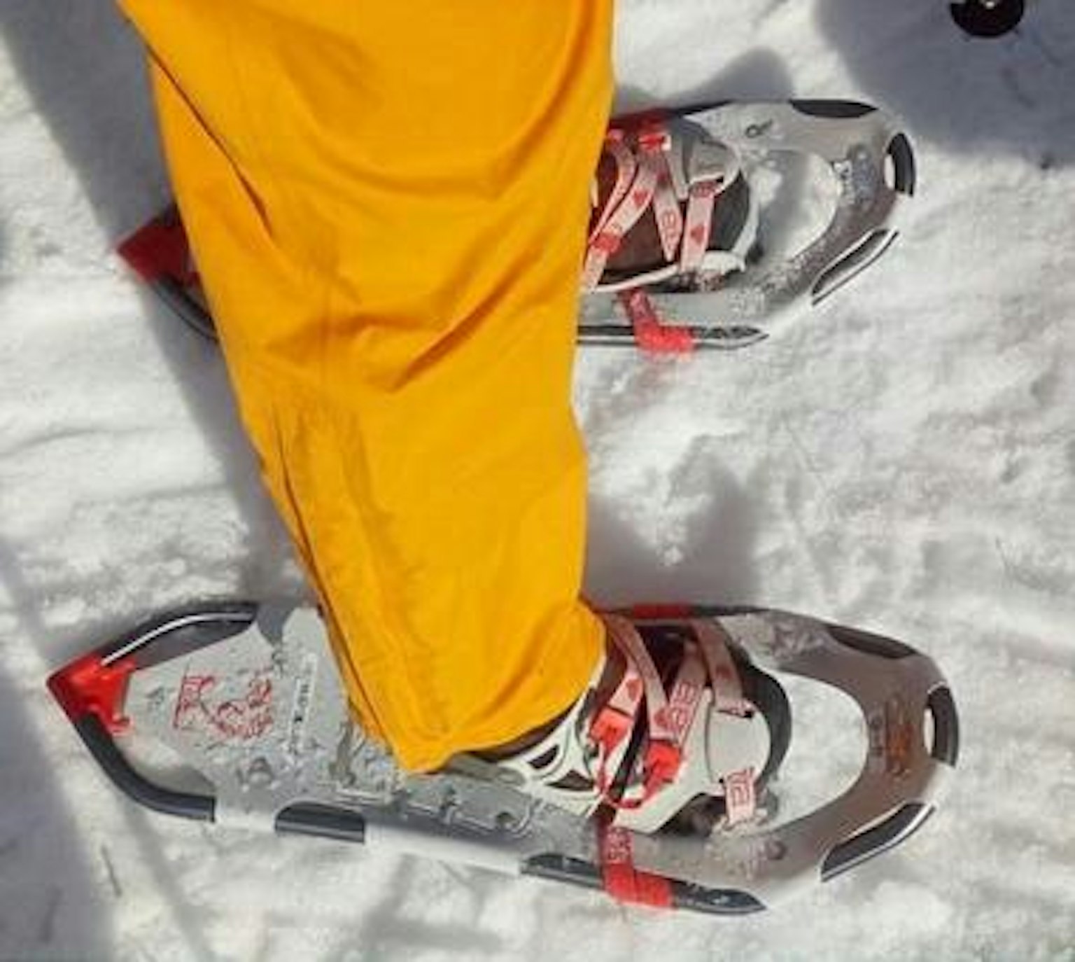 Piede in pantaloni gialli che sta sulla neve con racchetta da neve